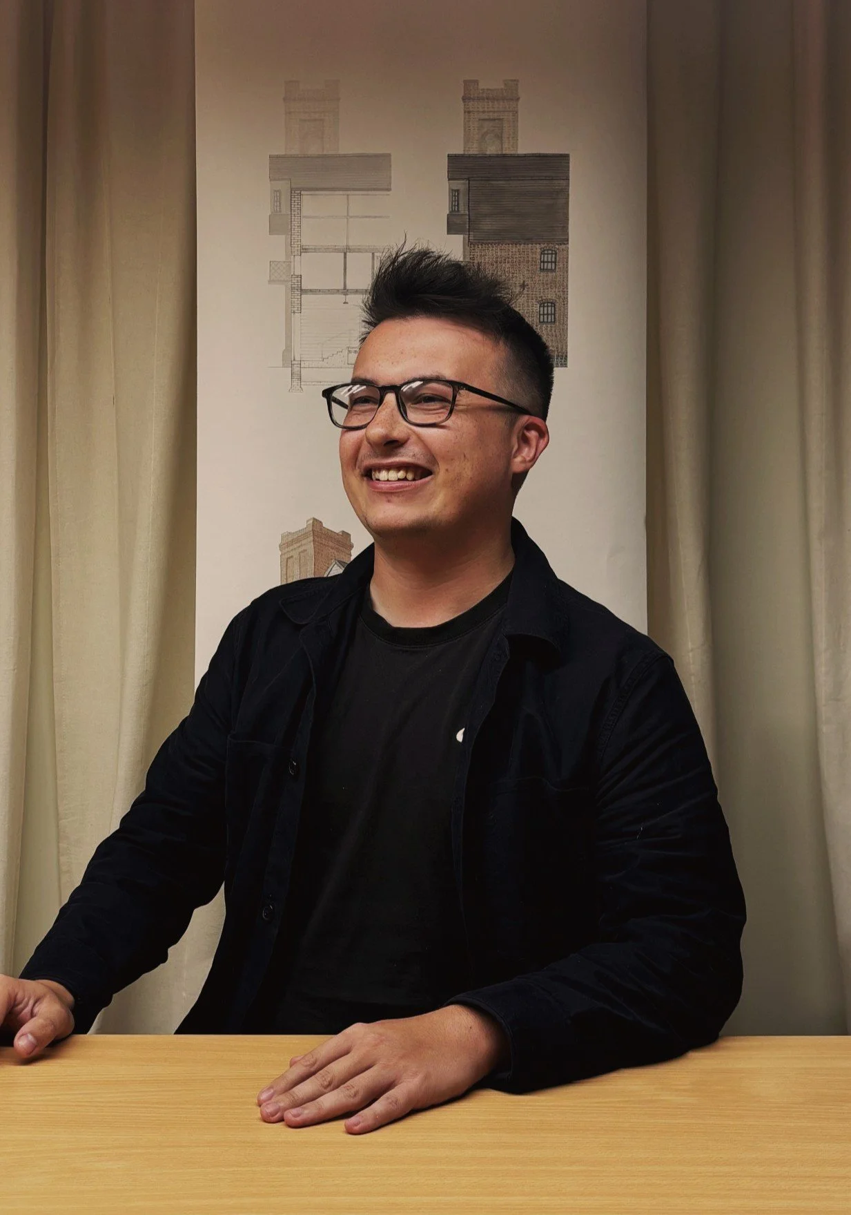 Our project architect smiling looking to the left hand ide of the room, wearing a black shit and hands on the table