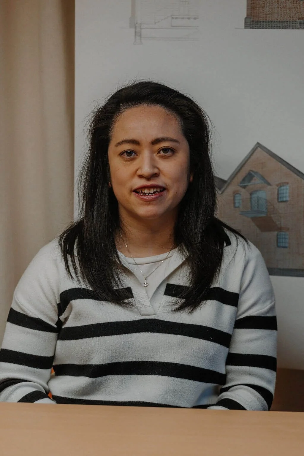 Winnie, wearing a black and white striped jumper, seated at a table with architectural plans behind them at the 24/Three studio