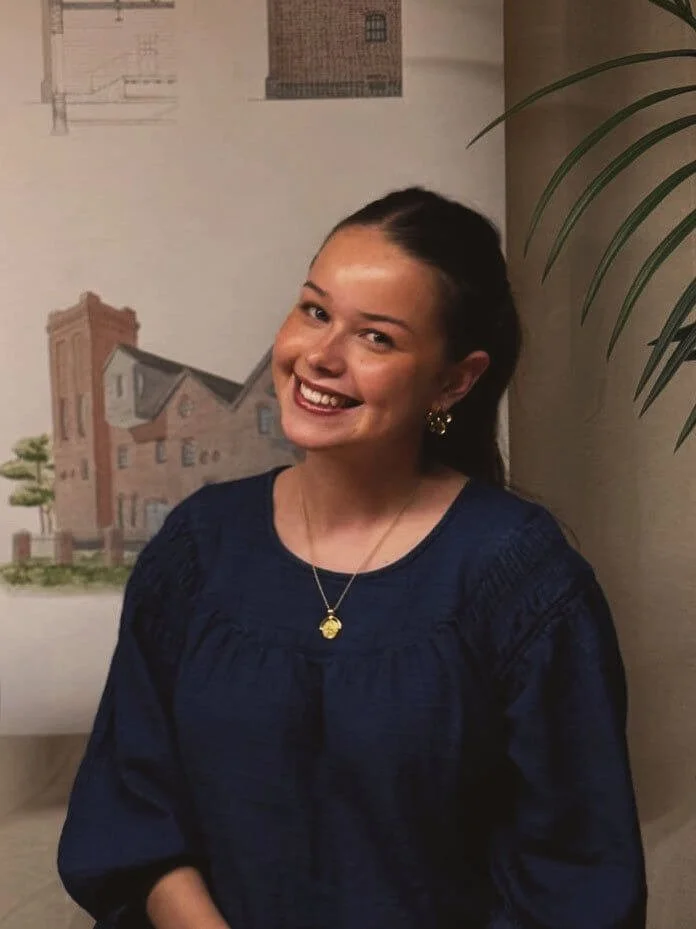 24/Three Poppy, Administrative Assistant, smiling at her desk