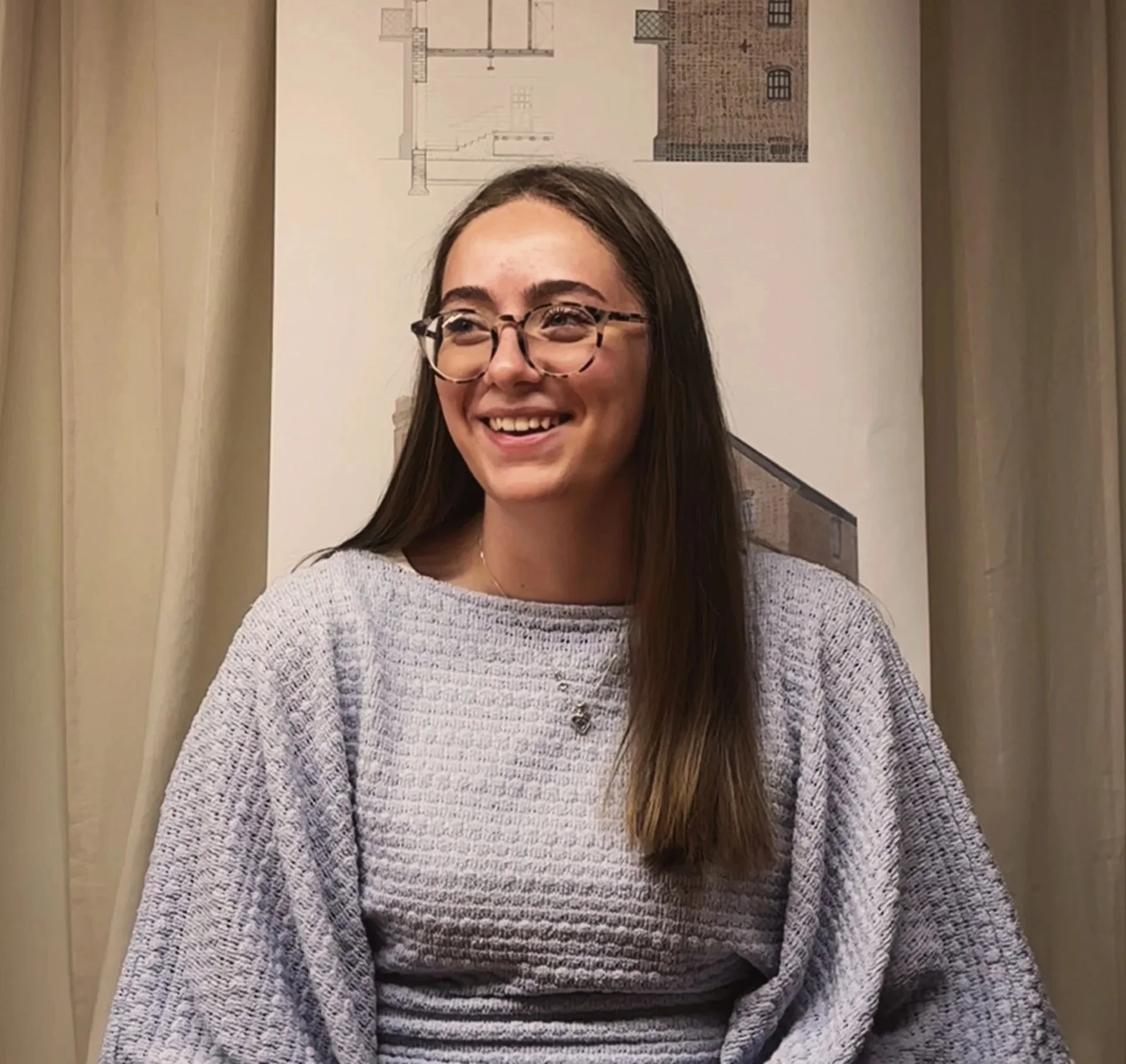 Jess Wright, our architectural assistant sitting in our newark office infornt of a watercolour background wearing a blue top