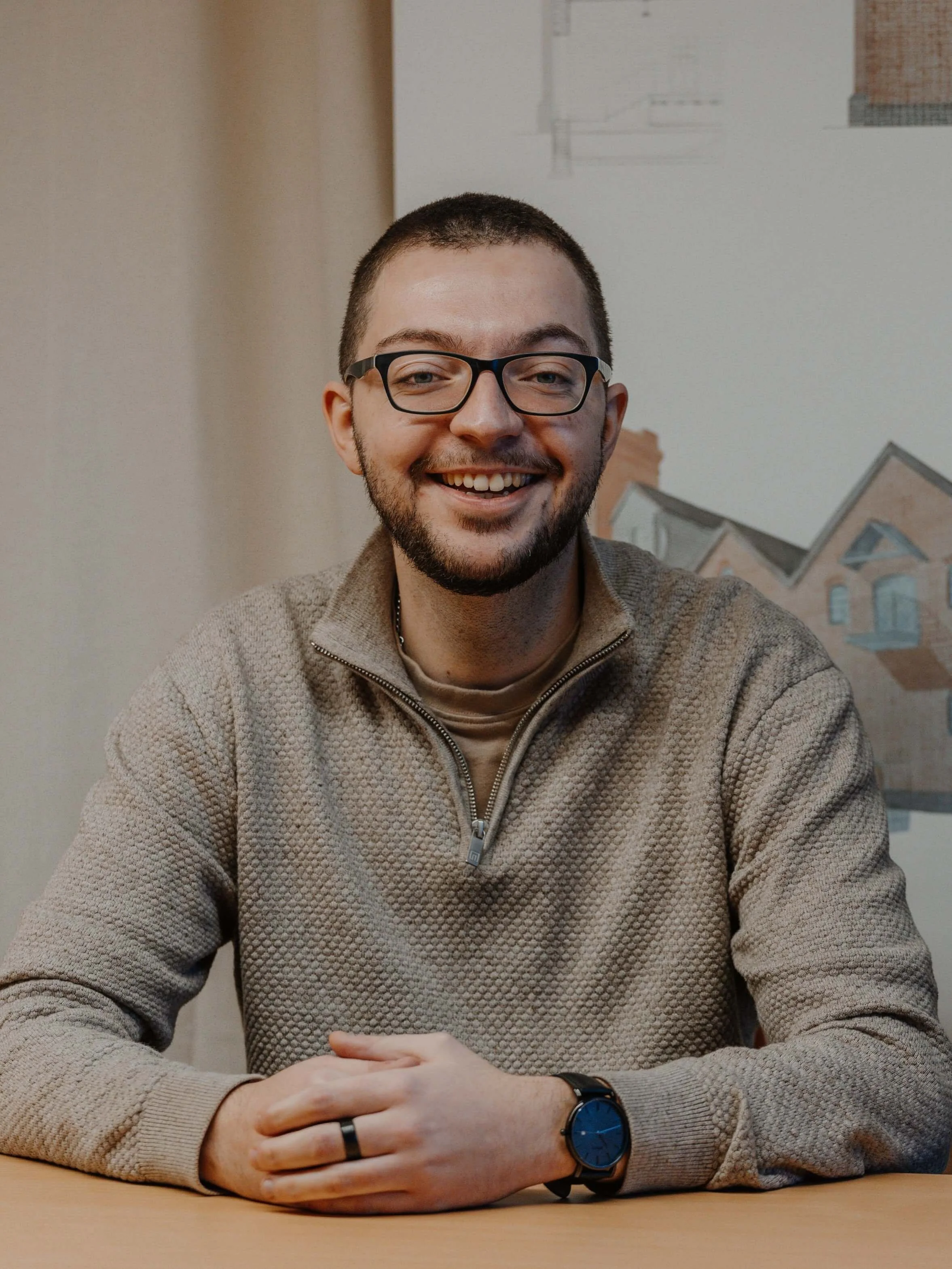 Shane, part of the 24/Three architectural studio team, smiling at a desk with drawings in the background