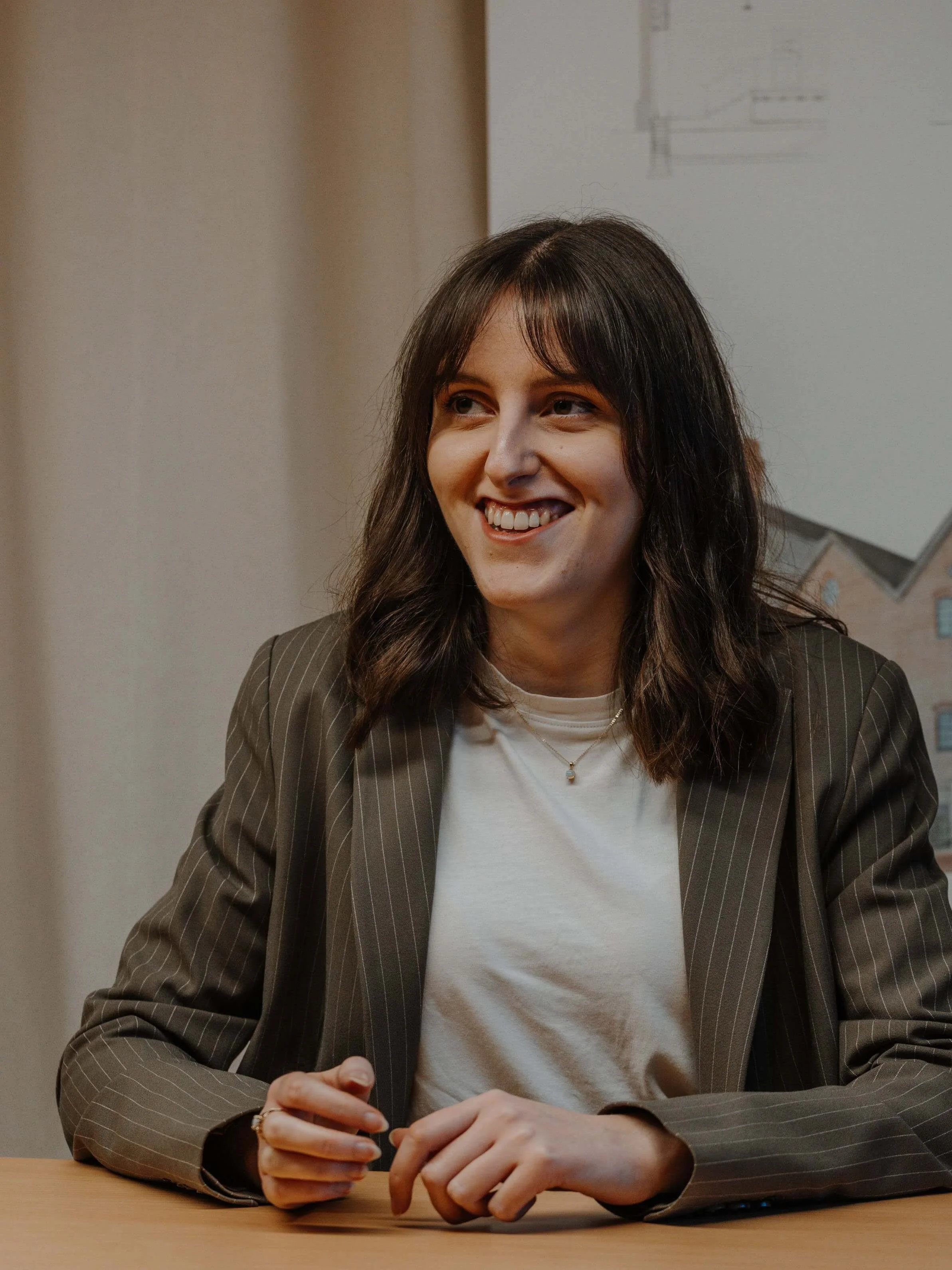 Philippa, part of the 24/Three architectural team, smiling at her desk in a pinstripe blazer and white shirt