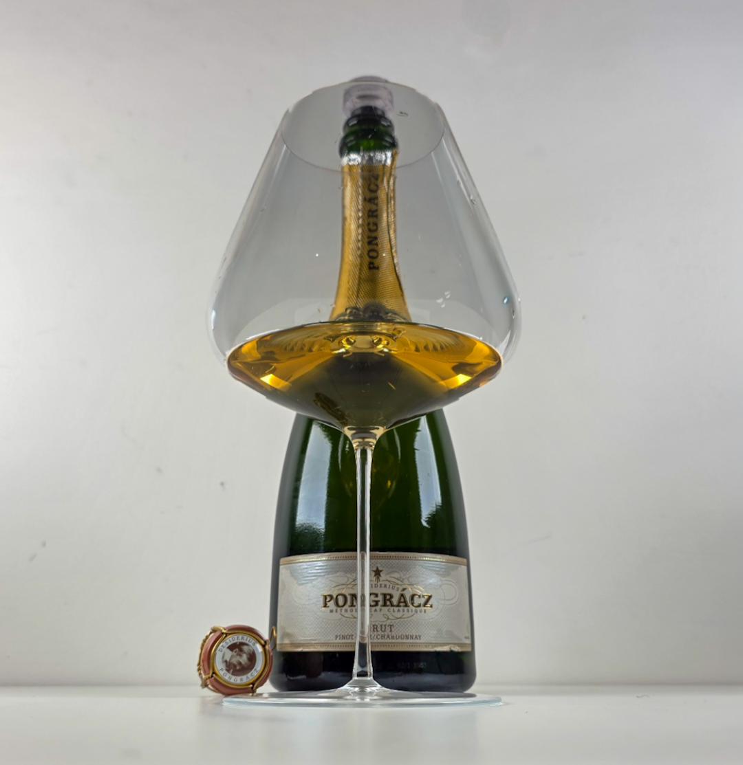 Still life of a Pongrácz Brut Cap Classique bottle and glass of sparkling wine against a white background