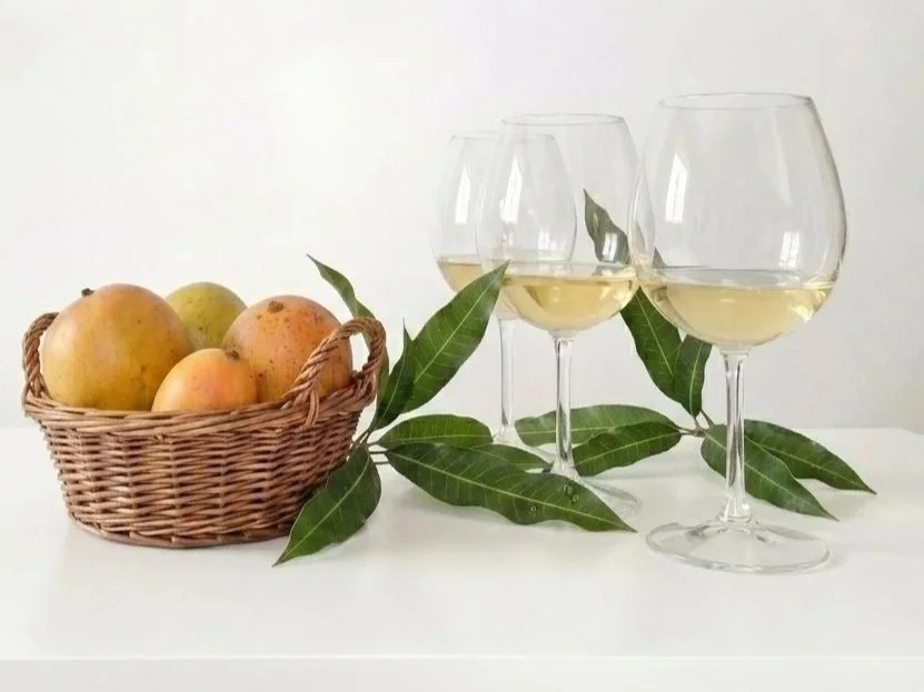 Three glasses of Viognier beside a basket of fresh Kenyan mangoes with mango leaves on a white table