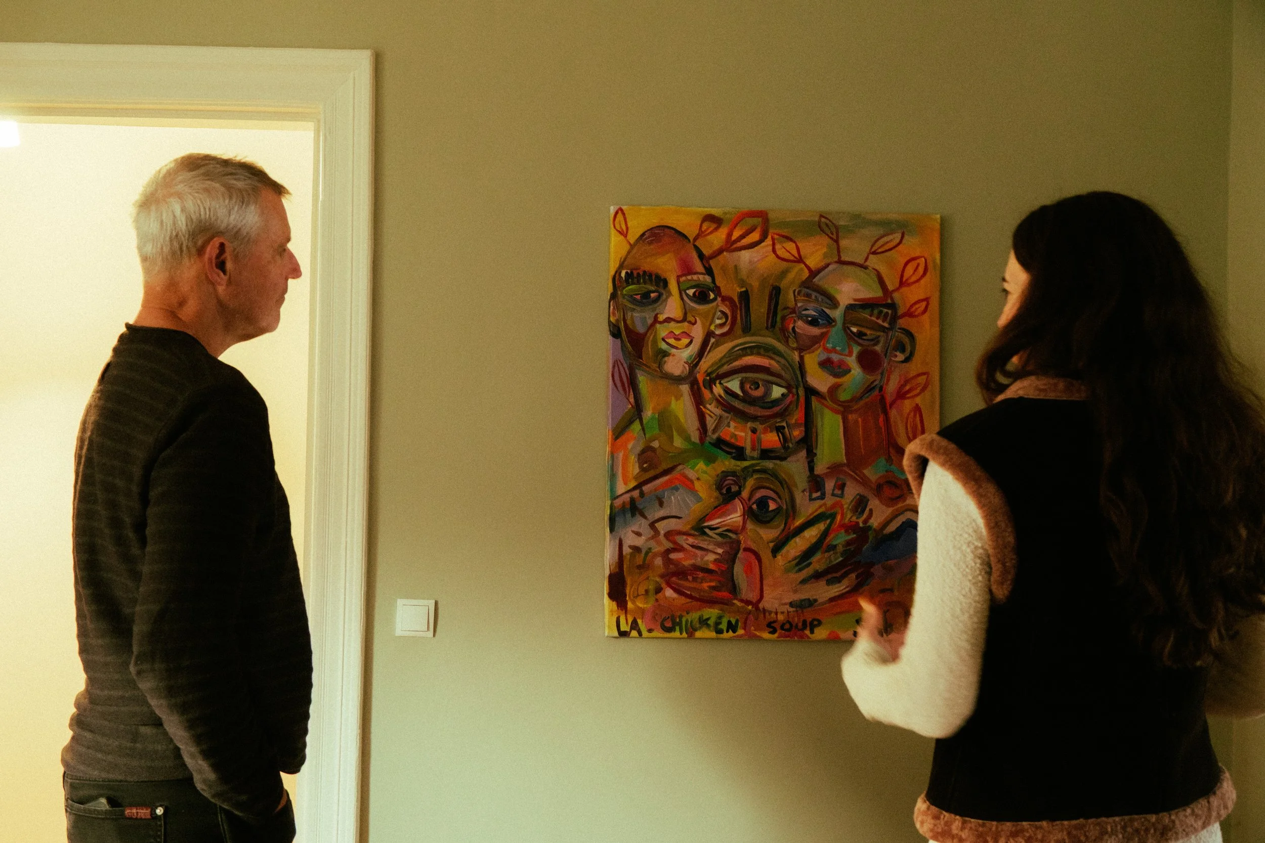 Two people looking at colorful abstract artwork on a wall.