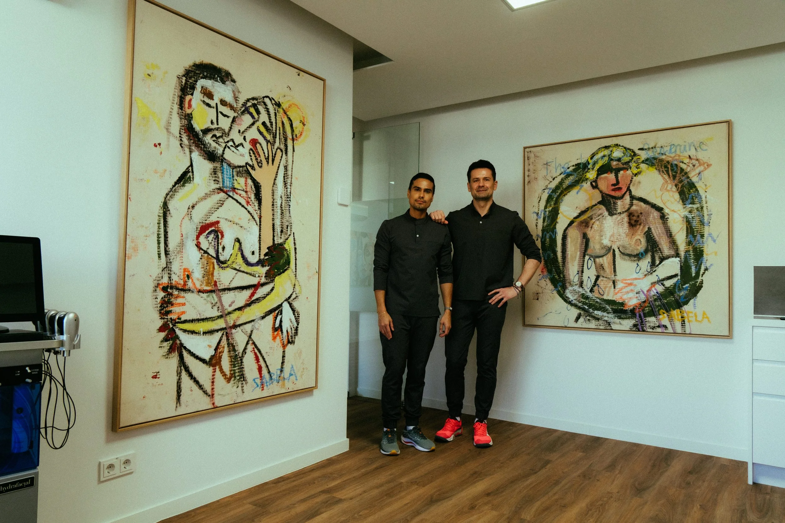 Two men standing in an art gallery with colorful abstract paintings on the walls.