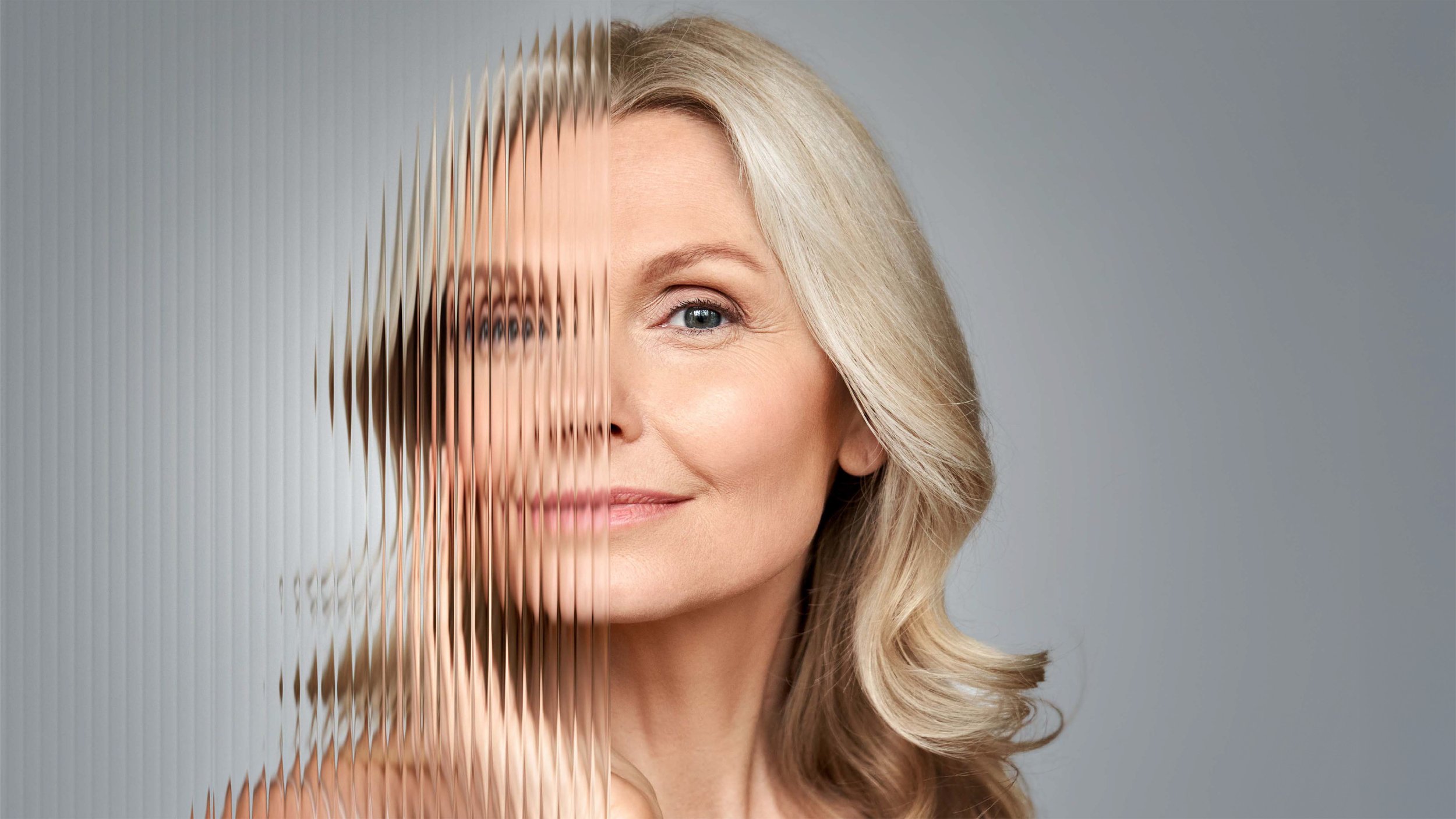 A woman with blonde hair and blue eyes smiling, with half of her face appearing through a textured, vertical mirror.