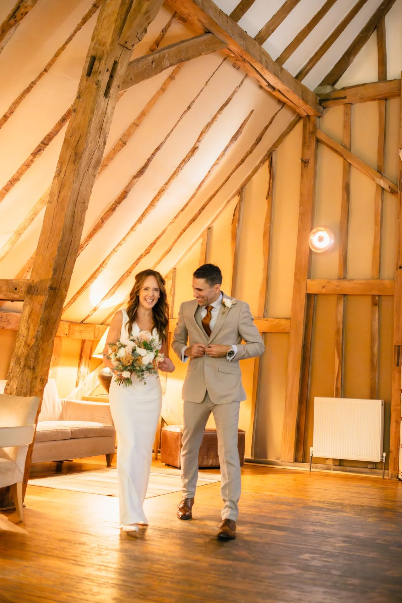 just-married couple laugh together as they had out to meet their guests at a barn wedding in essex by thomas bedwin