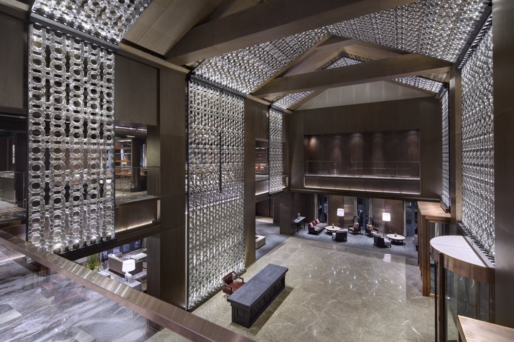 Interior view of a luxurious hotel lobby with high ceilings, decorative lighting, and modern furniture.