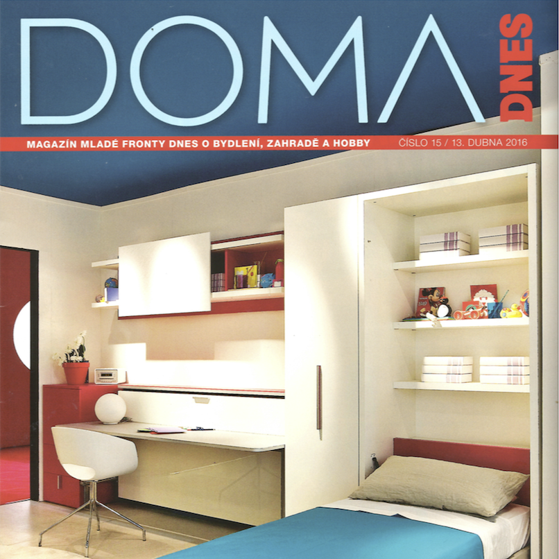 Interior of a bedroom with a white desk, a white chair, and a built-in white wardrobe with shelves filled with toys and boxes, a bed with a beige pillow and a blue bedspread, and a wall with a red bookshelf.