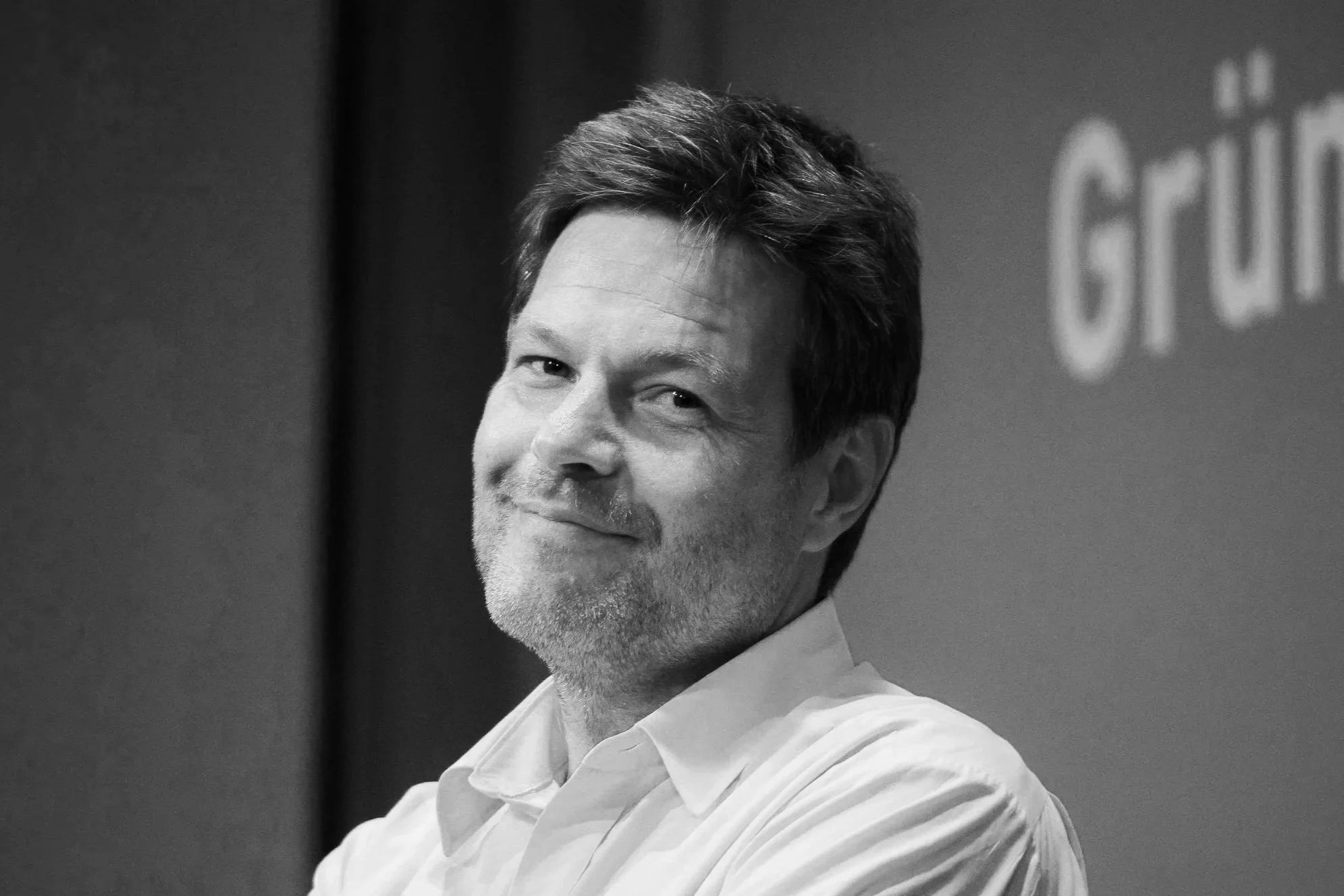 Schwarz-weiß Portrait eines Mannes mit dunklen Haaren, Augen, die zum Betrachter blicken, und einem leichten Lächeln, trägt einen weißen Hemdkragen.