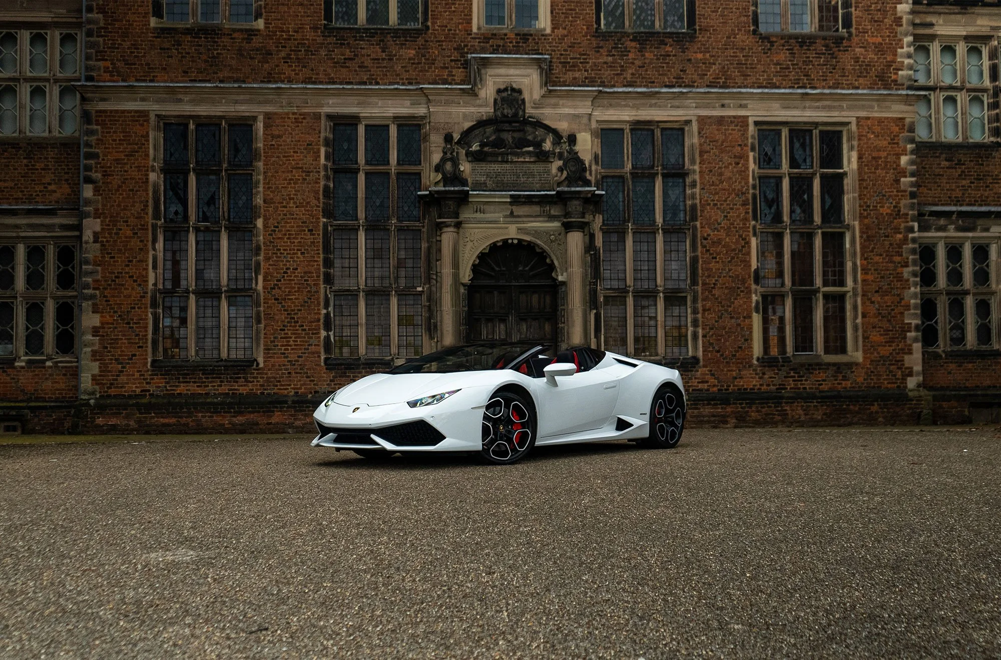 White Lamborghini parked in front of a historic brick building with large windows.