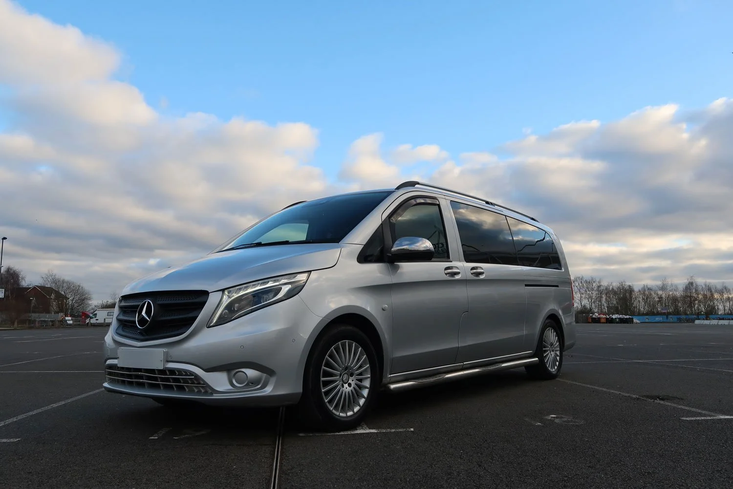 Silver Mercedes-Benz van parked in an empty lot under a cloudy sky.