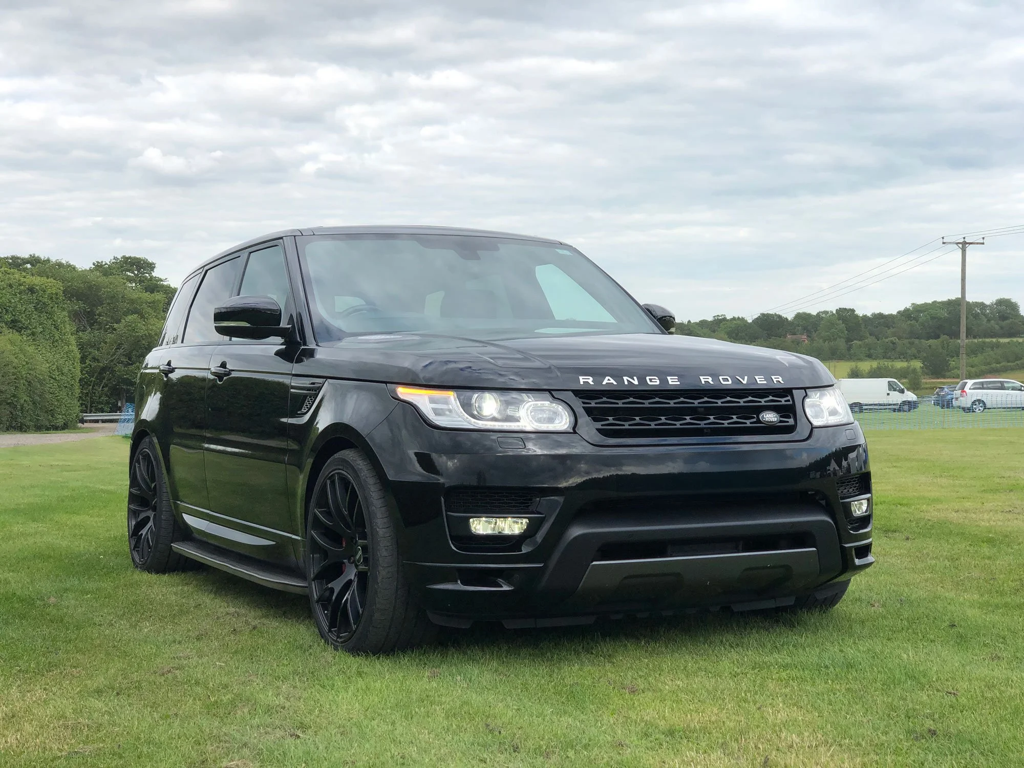 Black Range Rover parked on grassy field under cloudy sky.