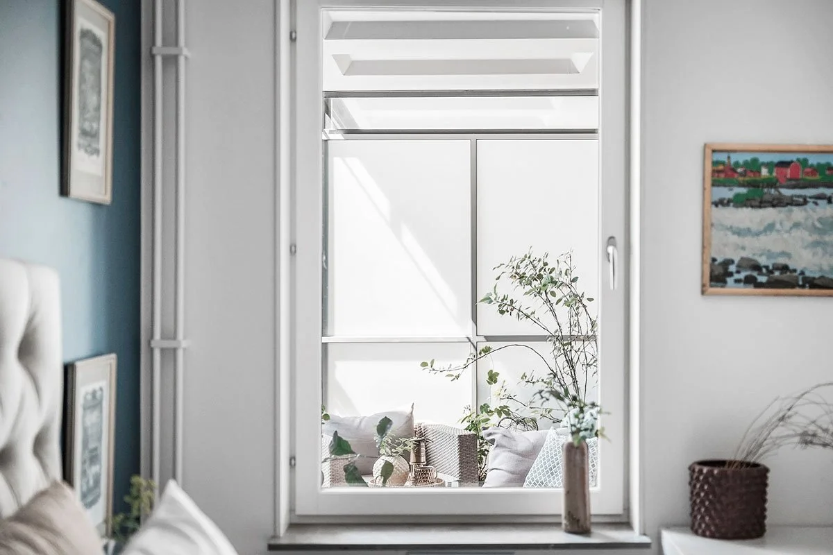 Homestyling Lidingö. Ljust sovrum med tavlor, fönster och blommor