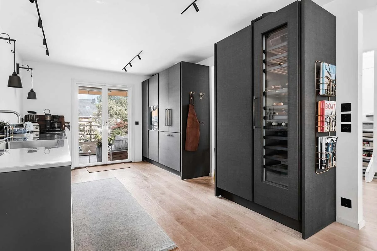 Homestyling Lidingö. Modernt kök med mörka högskåp, takbelysning och vinkyl