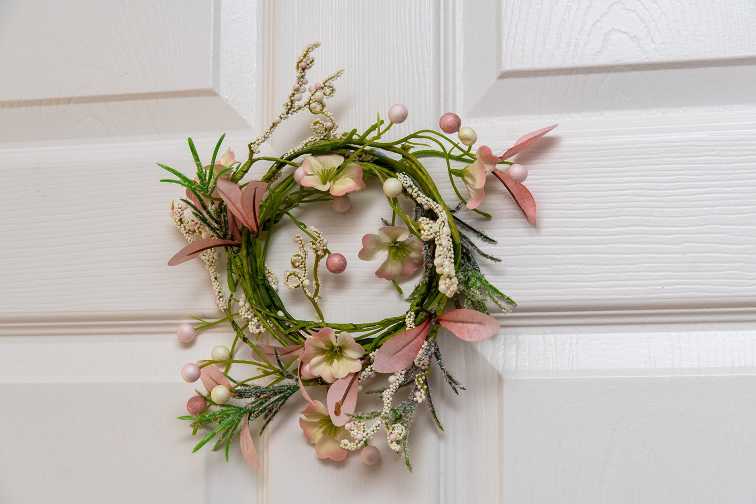 Decorative floral wreath with pink and white flowers on a white door.