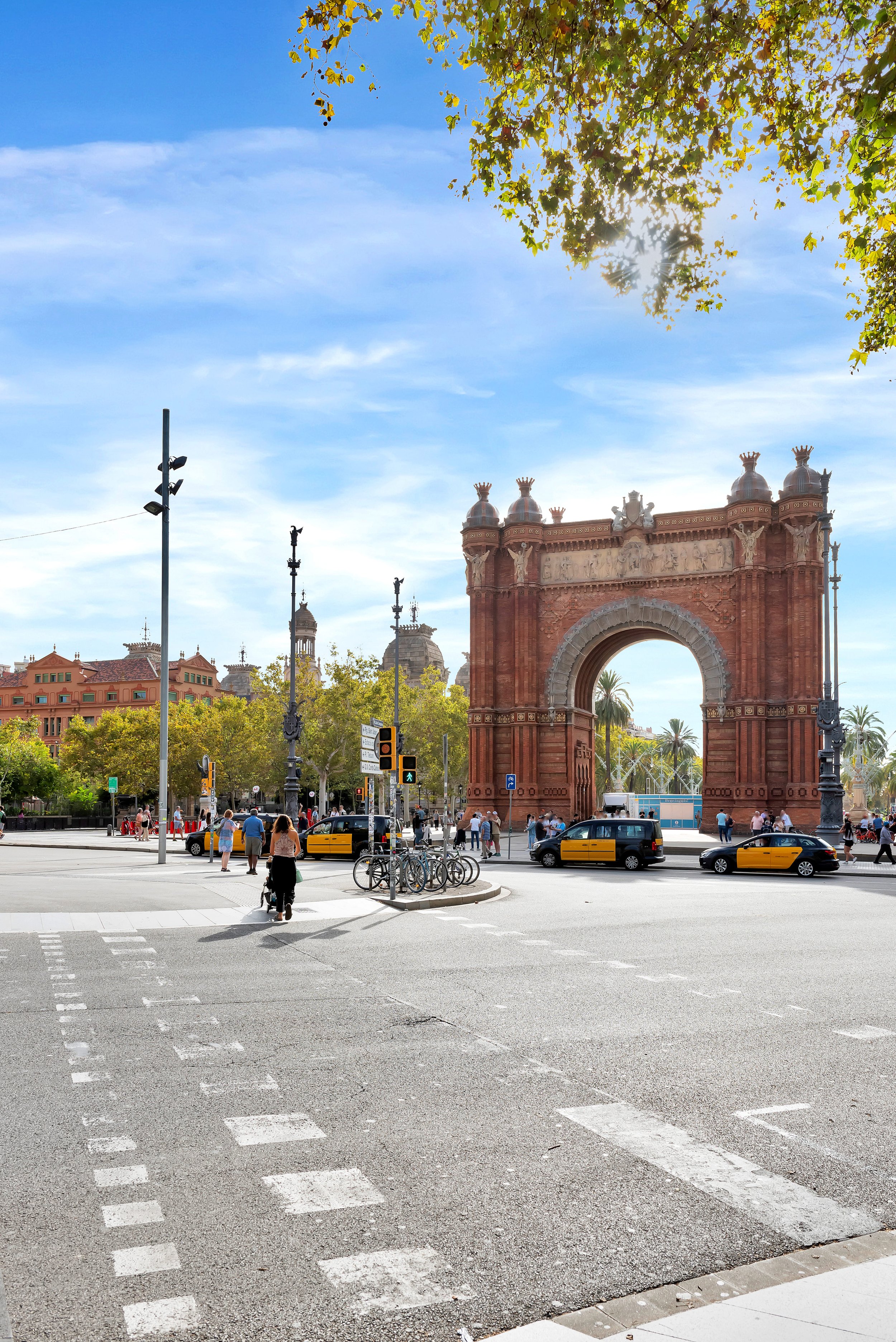 Arco de Triunfo en una plaza concurrida con taxis y peatones, árboles y edificios en el fondo, cielo despejado.