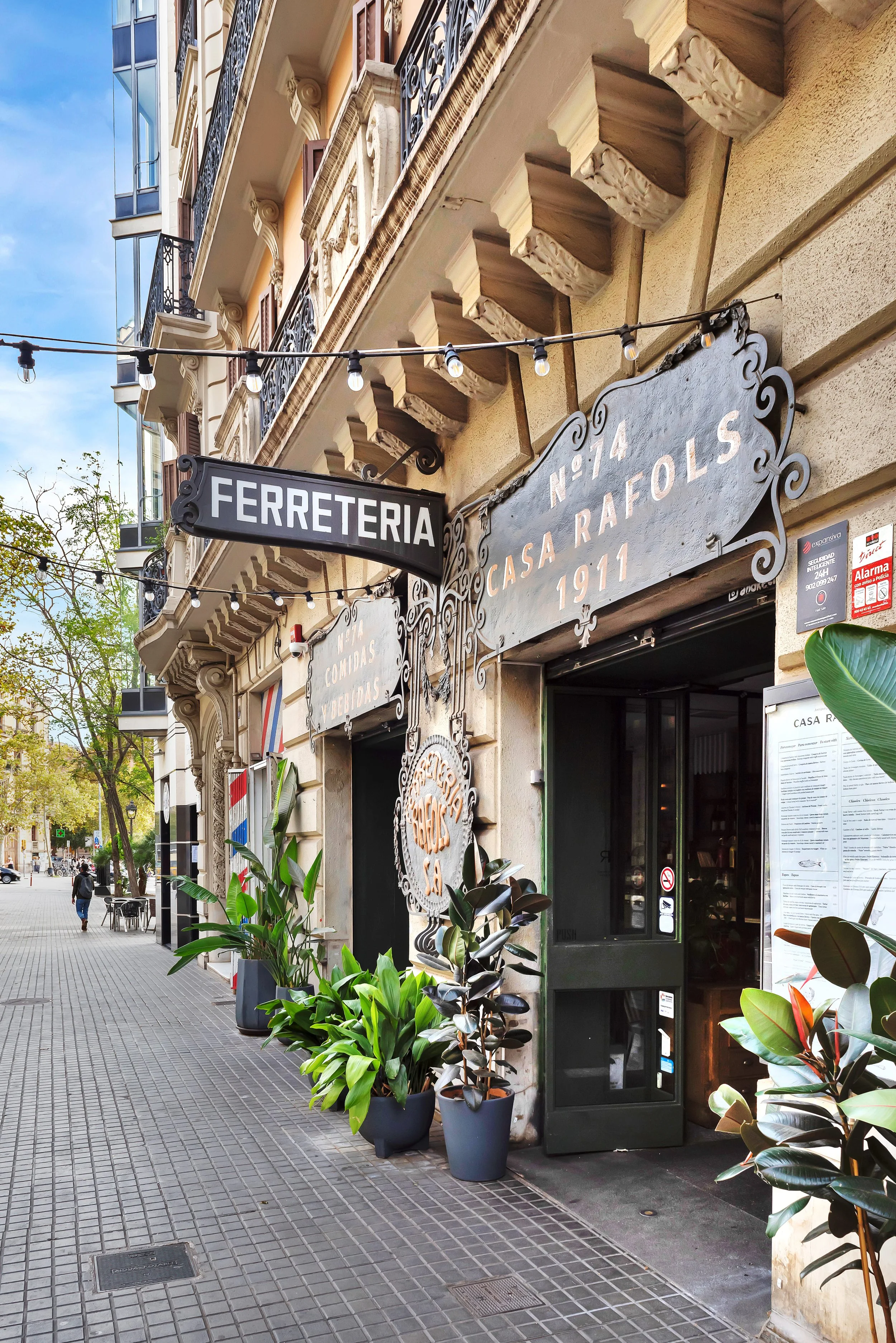 Fachada de una ferretería en una calle peatonal con plantas en macetas y un cartel que dice 'Ferretería'.
