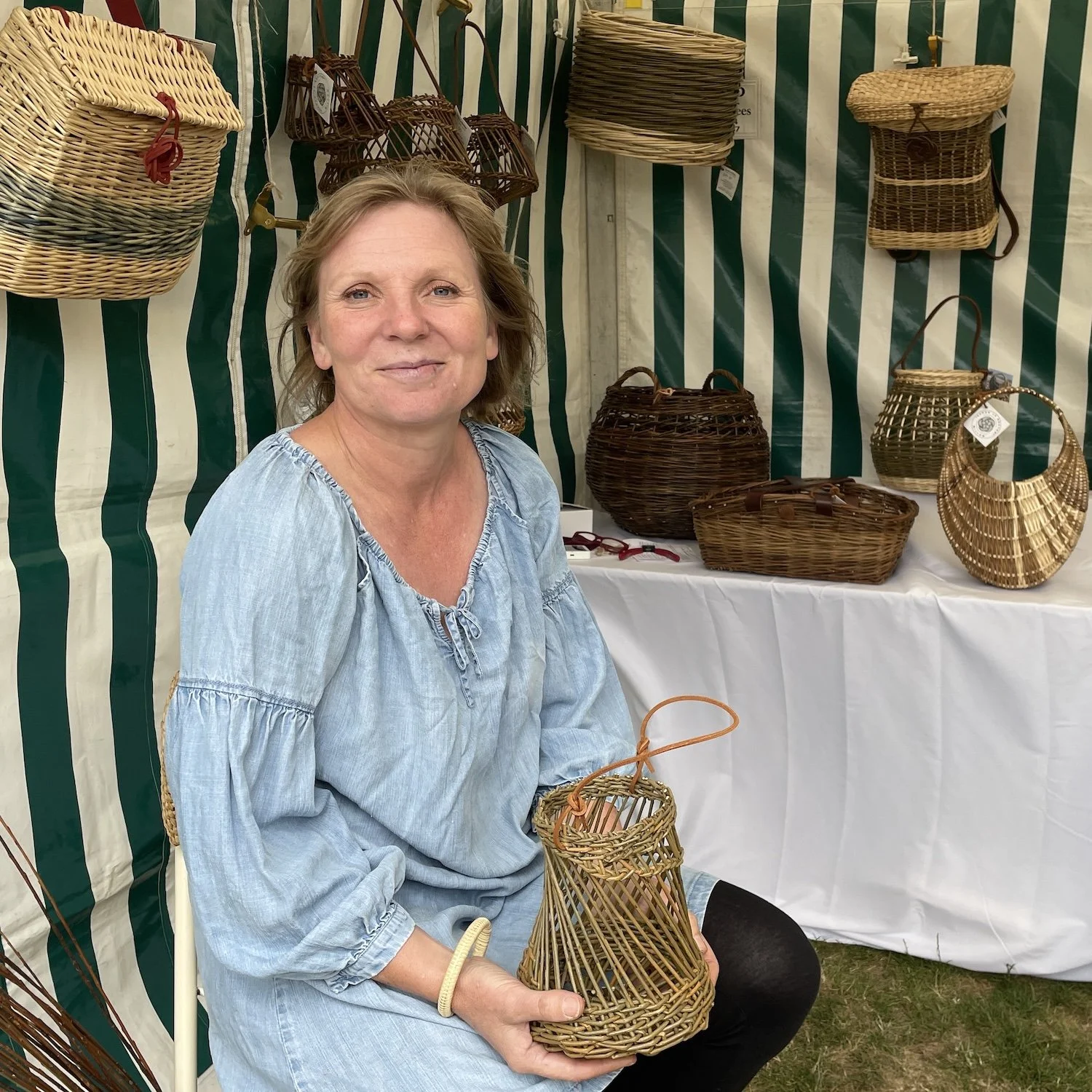 Sarah Le Breton sitting in front of range of colourful willow baskets handbag creel backpacks drum lampshade