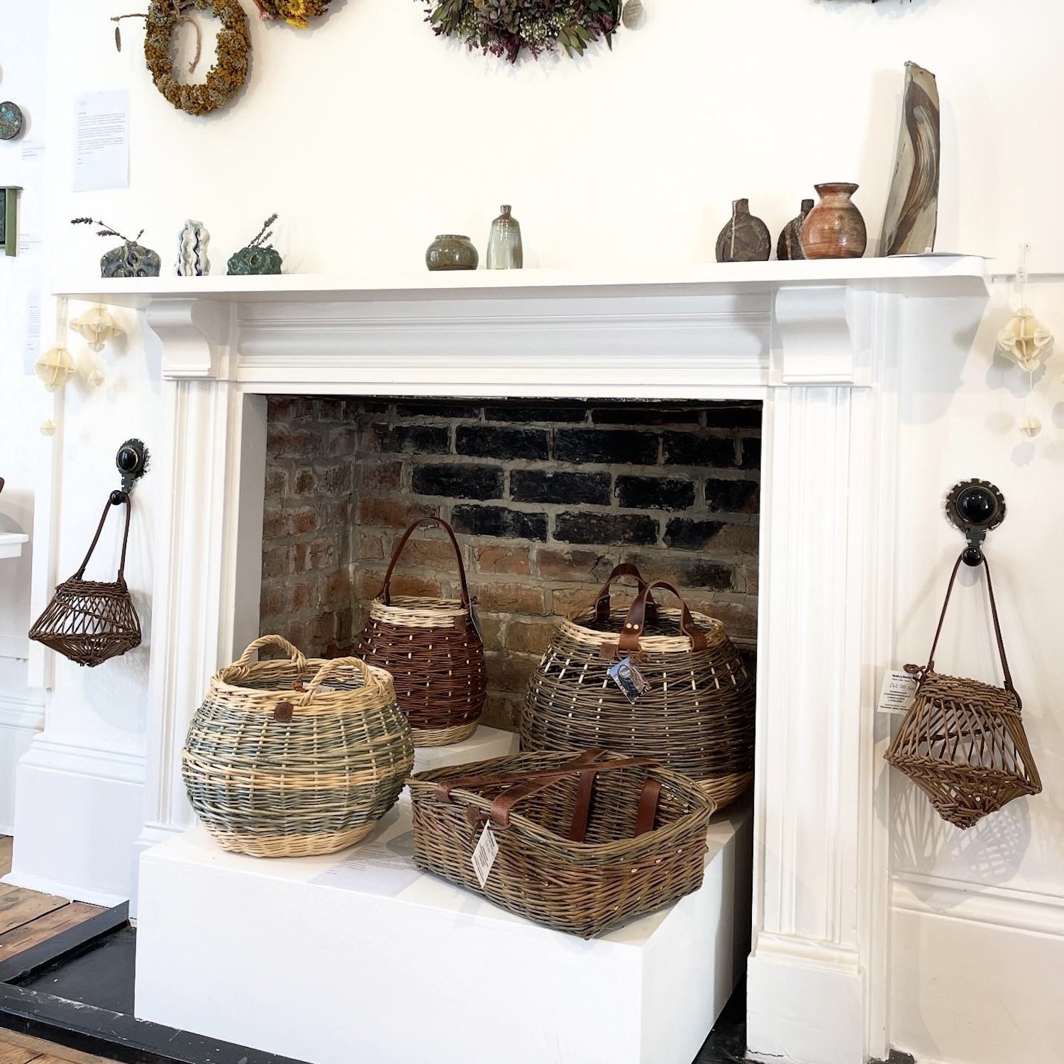Willow basket collection including feature round basket, rectangular garden basket trug, fruit baskets, blue and white indigo dyed round basket in front of woodburner
