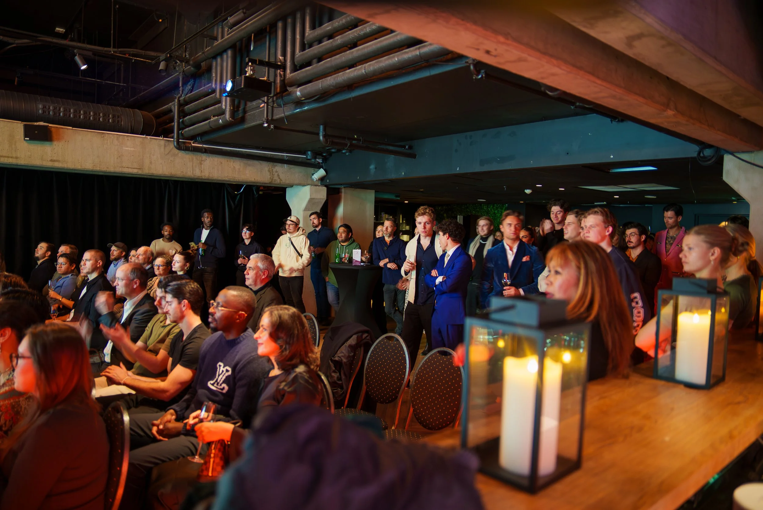 Mennesker i en konferansesal, noen står og snakker, mange sitter og ser på, noen med glass i hånden. Stemningen er formell og oppmerksom.