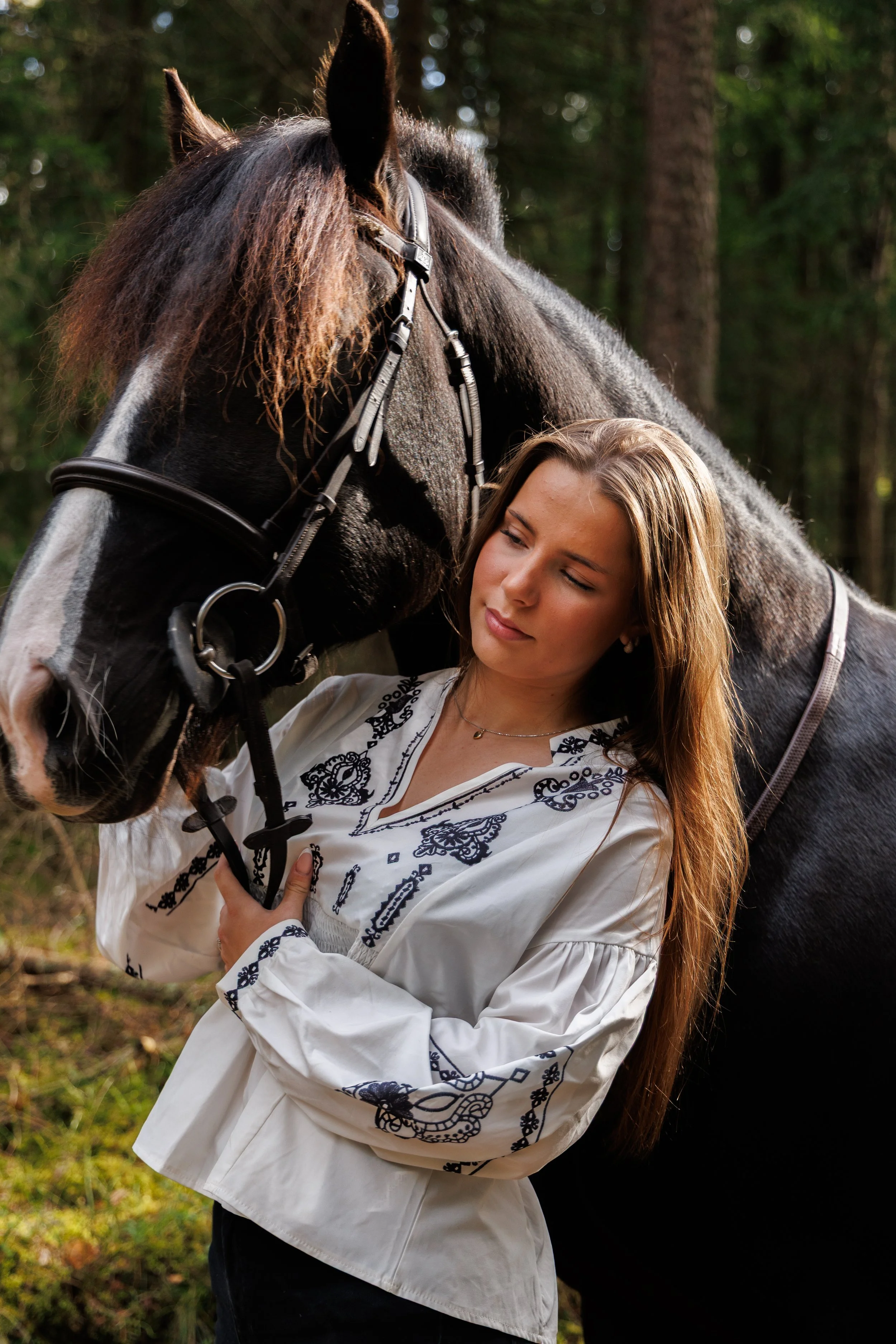En kvinne holder i biten av en hest i en skog.