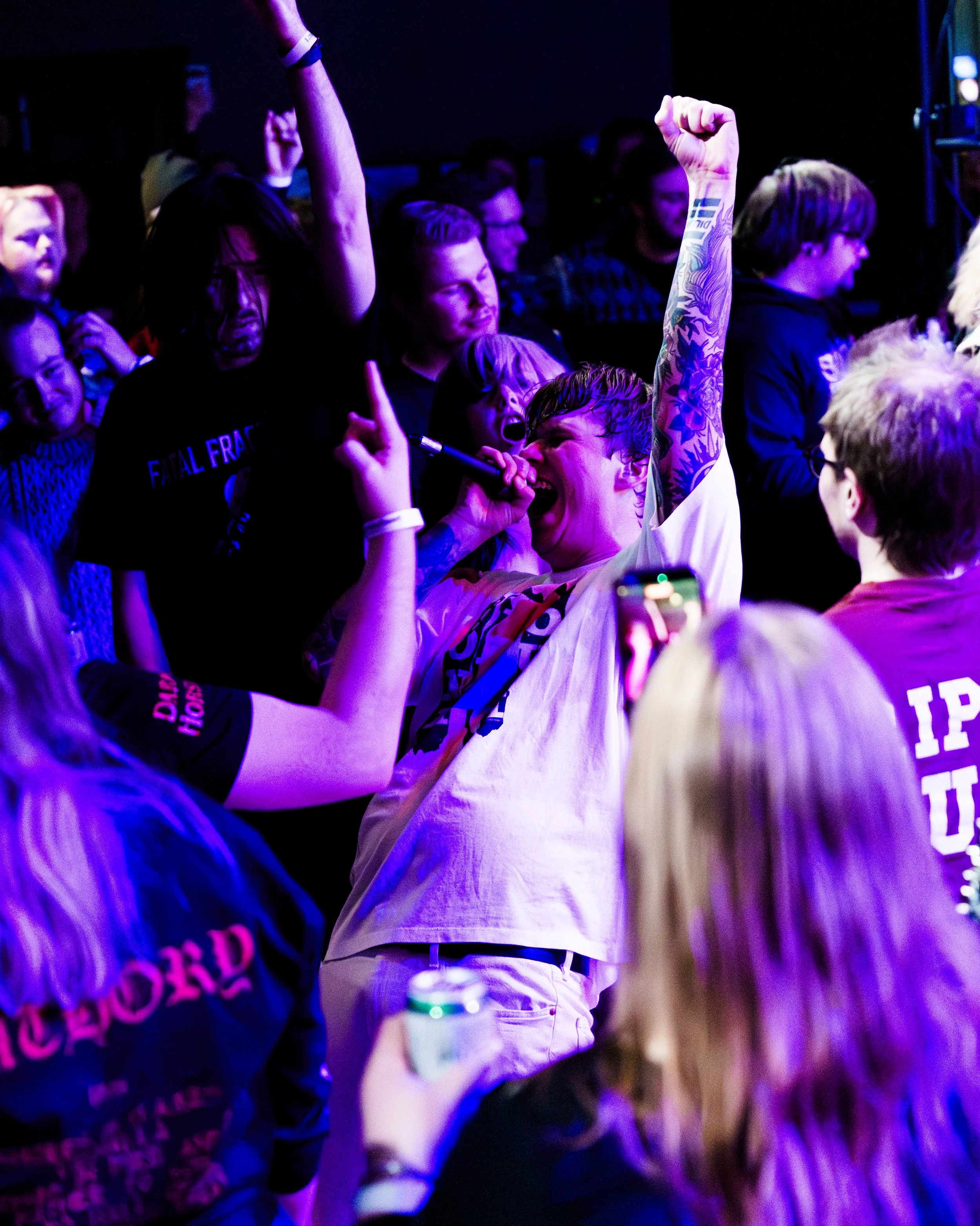 Person som synger med mikrofon i en crowd under konserten, med armene løftet.
