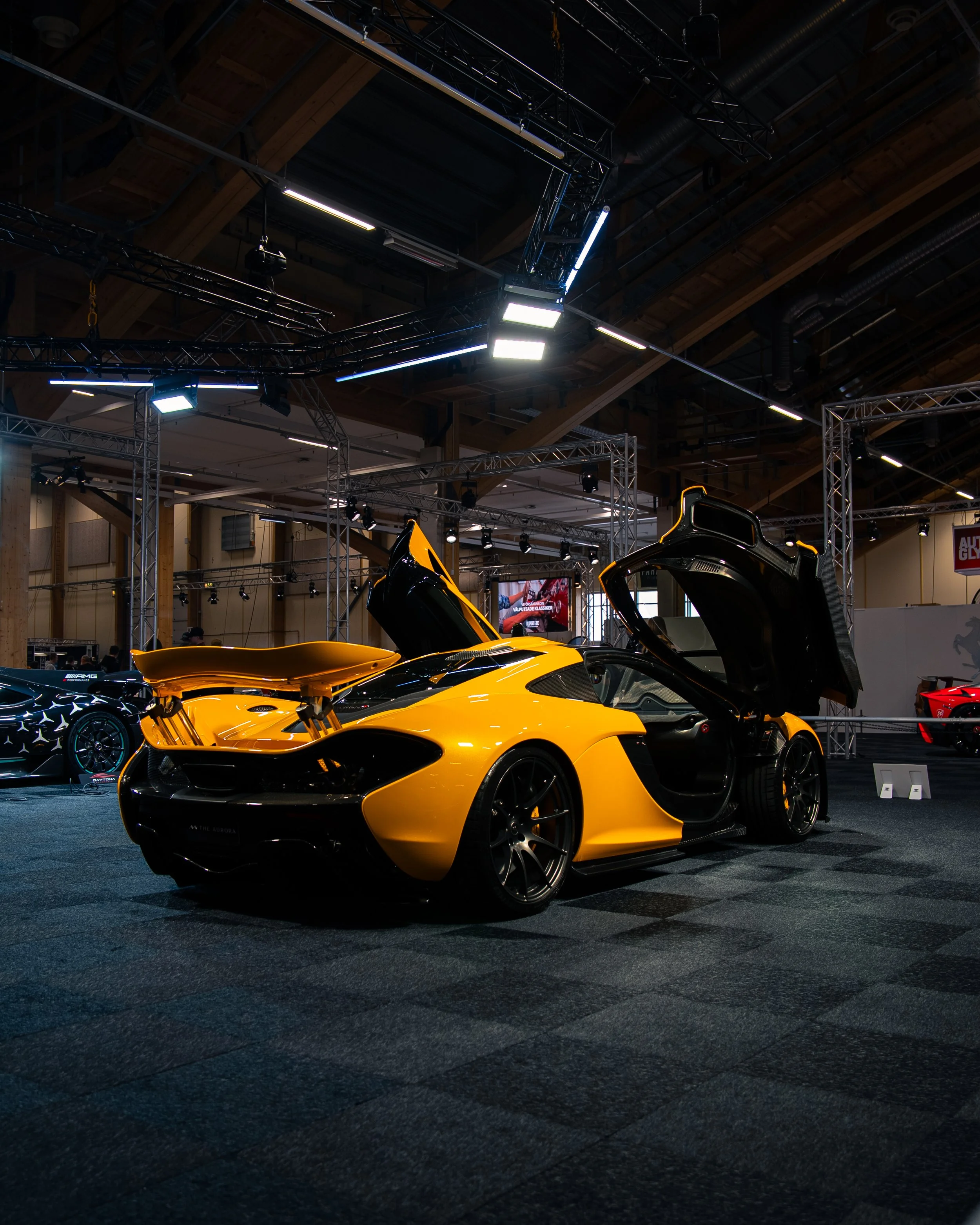 En gul og svart sportsbil med oppløftede dører vist på en bilutstilling.
