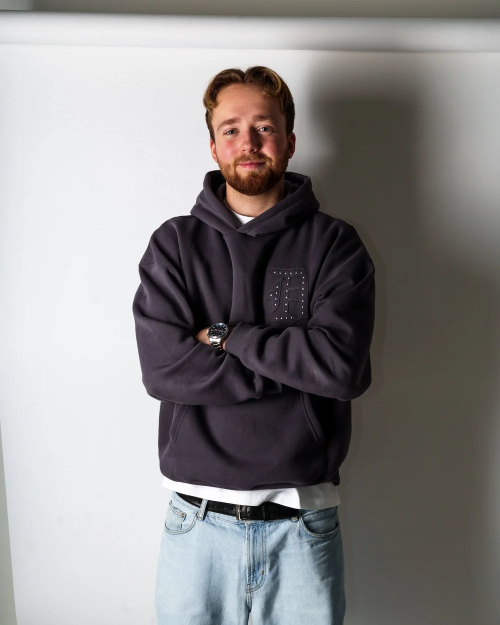Portrett av person i hettegenser mot lys vegg i studio