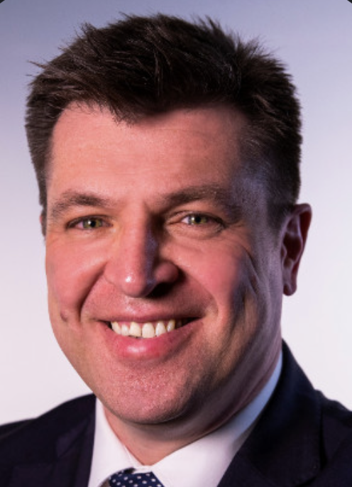 A smiling man in a suit with light skin and short, dark hair.