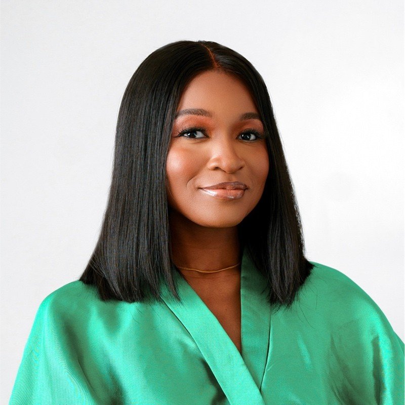 A woman with straight black hair, wearing a green satin blouse, smiling slightly, against a plain white background.