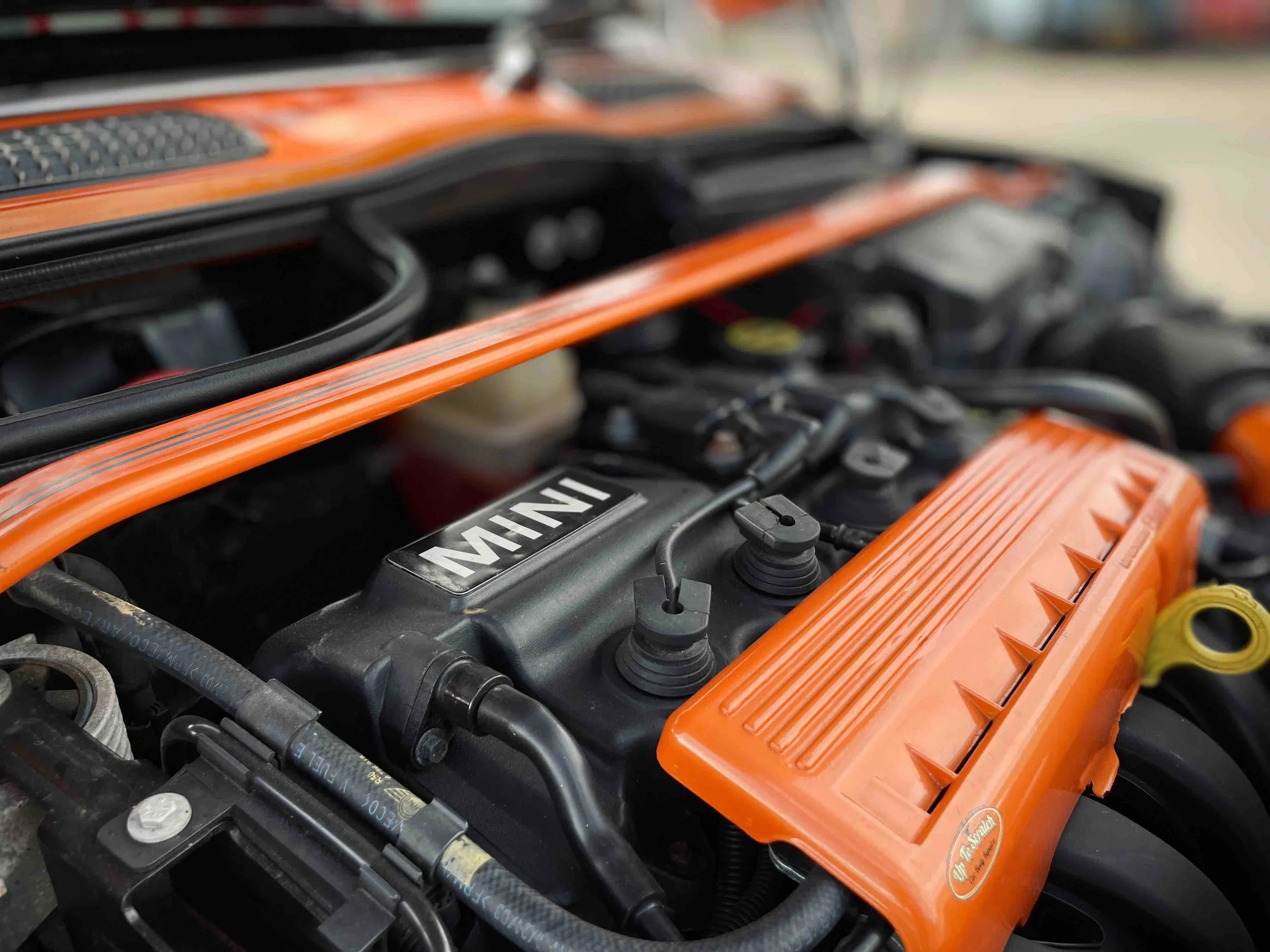 Close-up of a Mini Cooper engine with orange valve cover and black engine components.