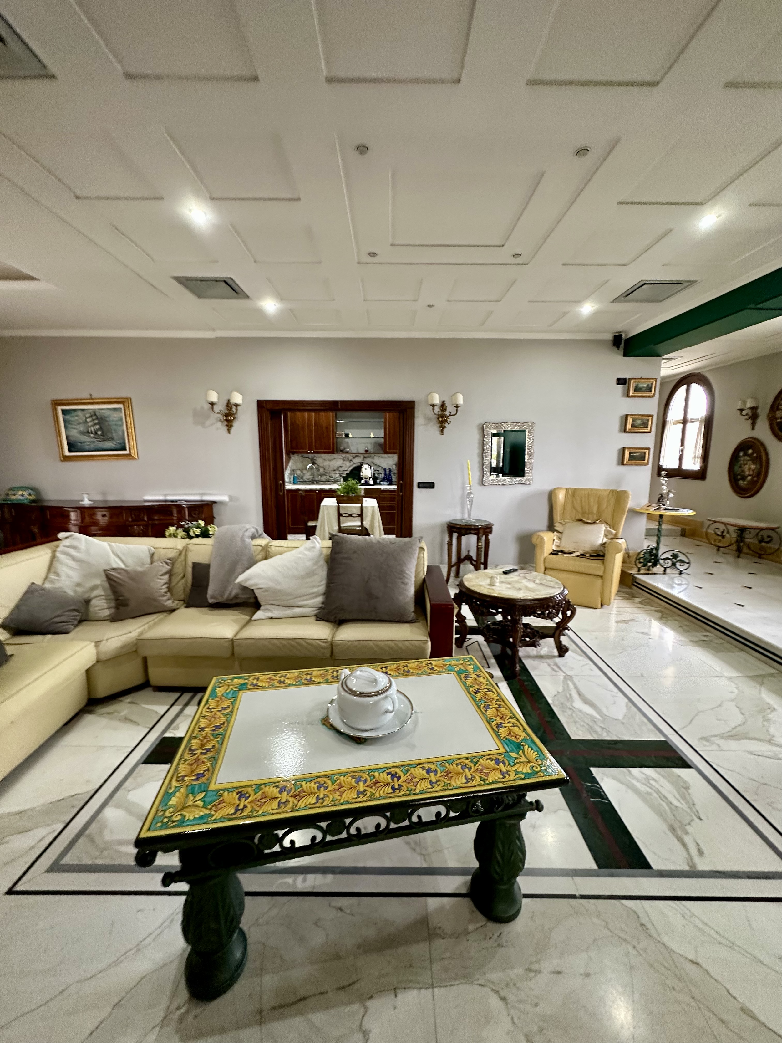 Luxurious living room with a sectional sofa, decorative tiled coffee table, marble flooring, wall art, and elegant lighting.