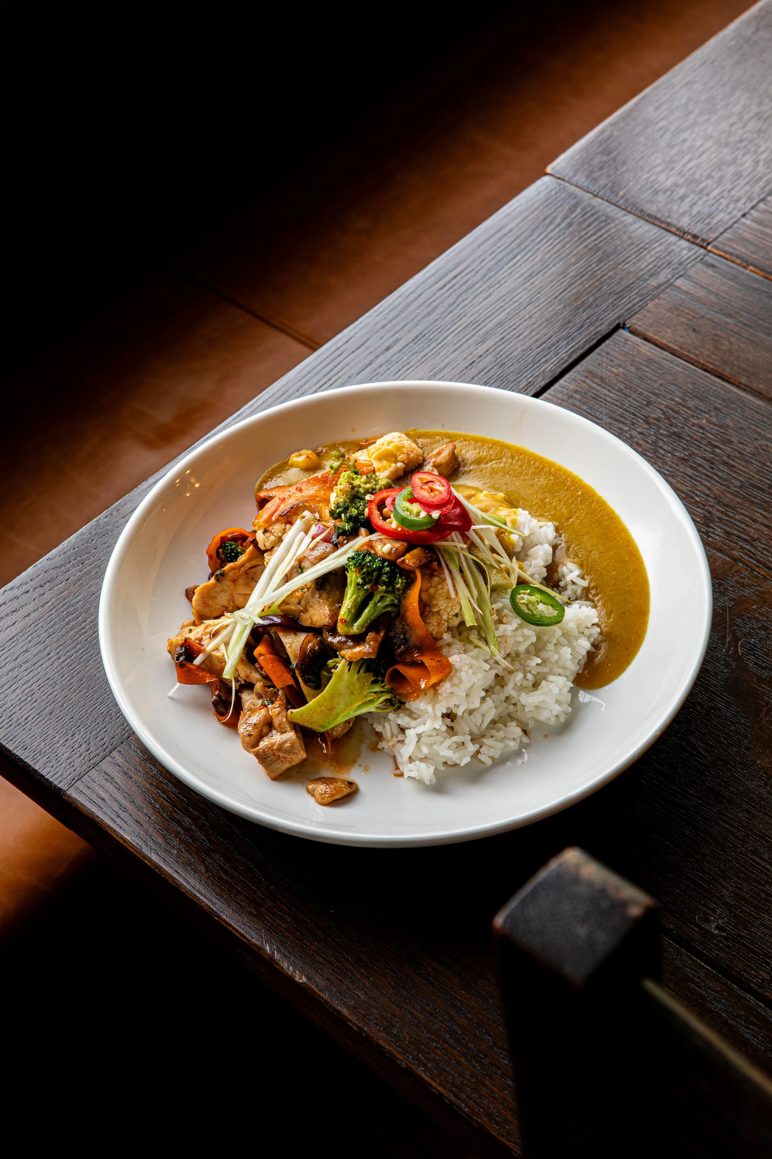 Plate with white rice, stir-fried vegetables, and curry on a dark wooden table.