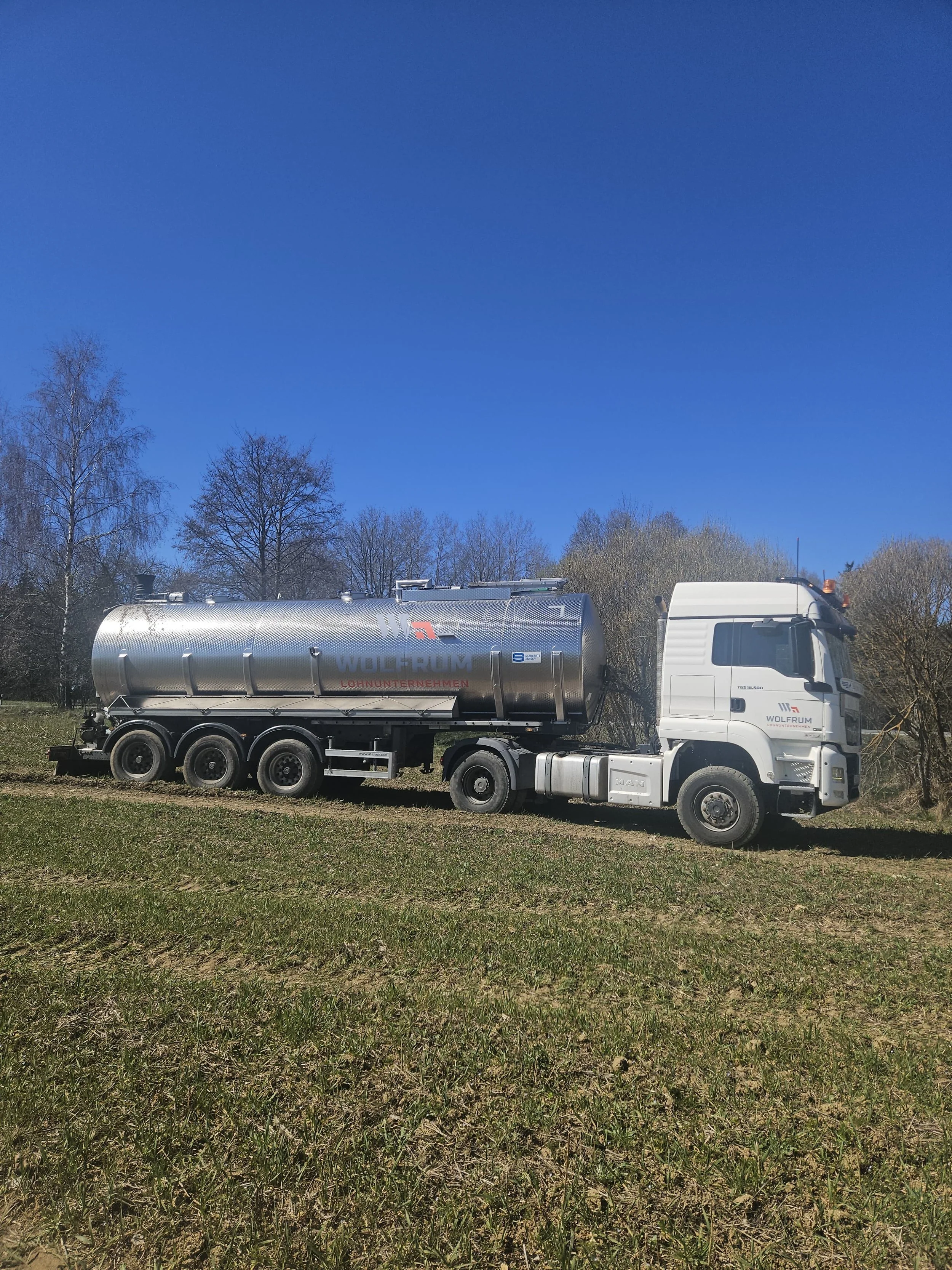 LKW mit Tankwagen-Auflieger auf einem Parkplatz, weitere LKWs im Hintergrund, der Himmel ist bewölkt.