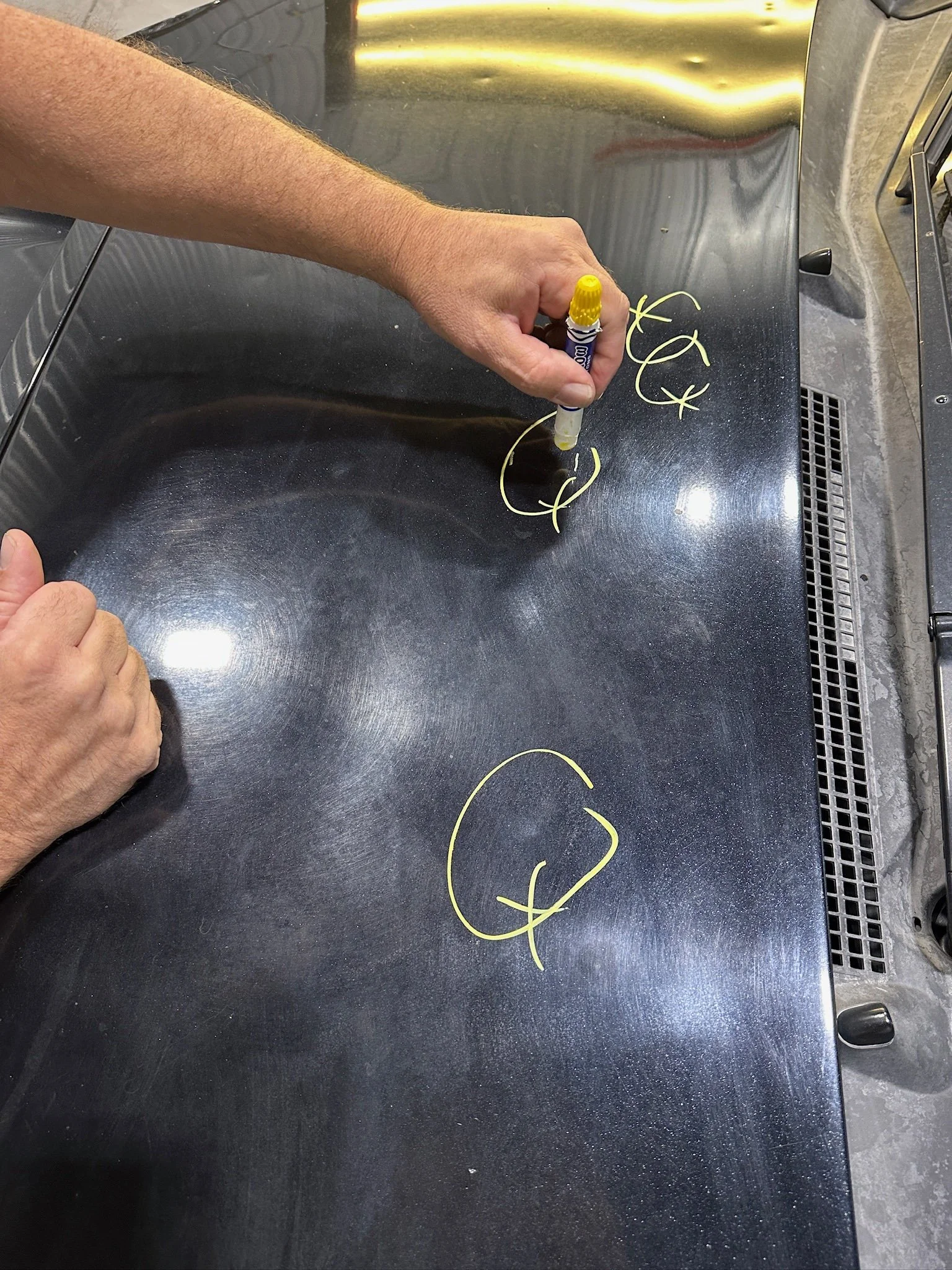 Person circling dents on the hood of a car to prepare for paintless dent repairs
