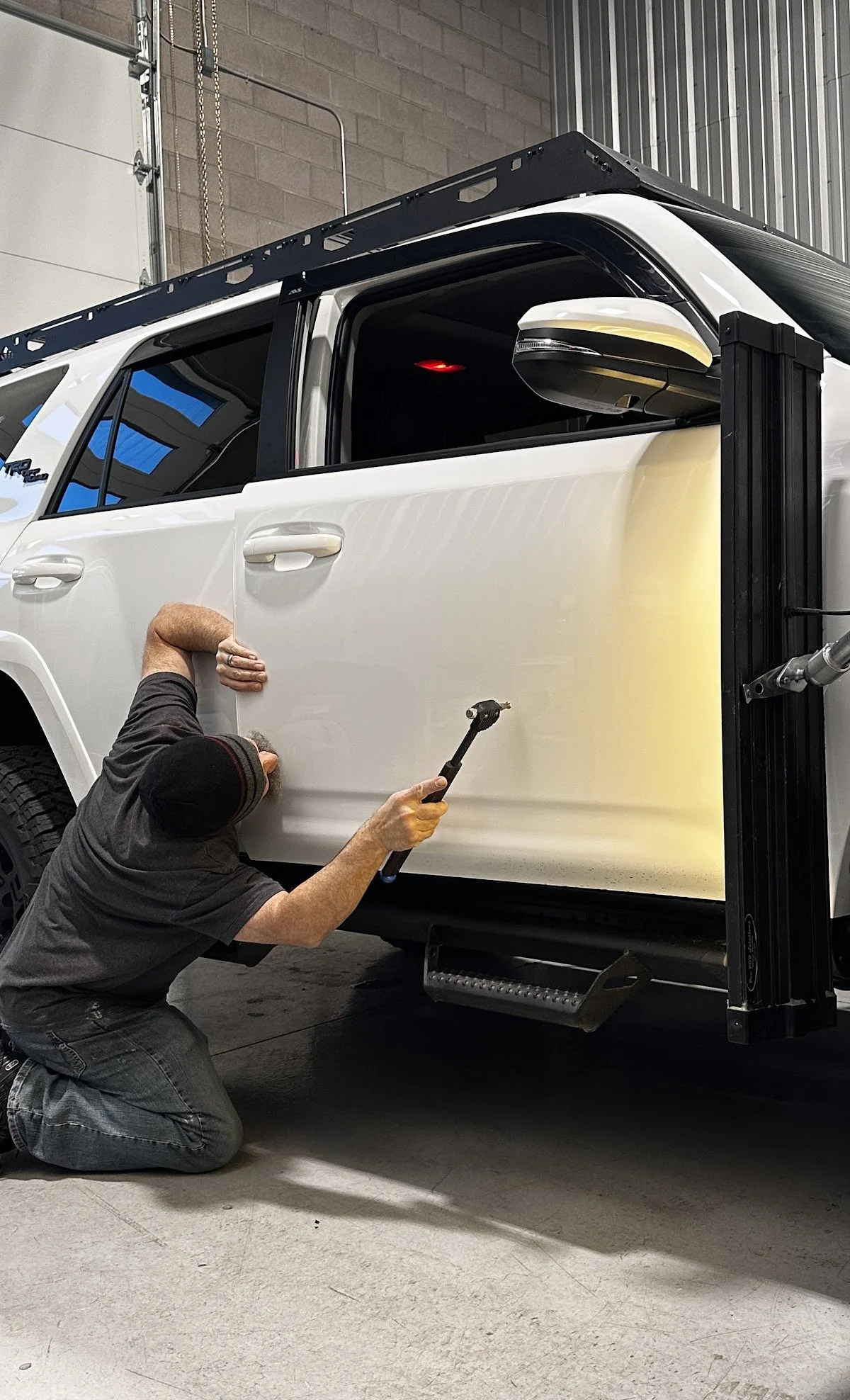 Person working on a white vehicle, using a tool on the door for paintless dent repair