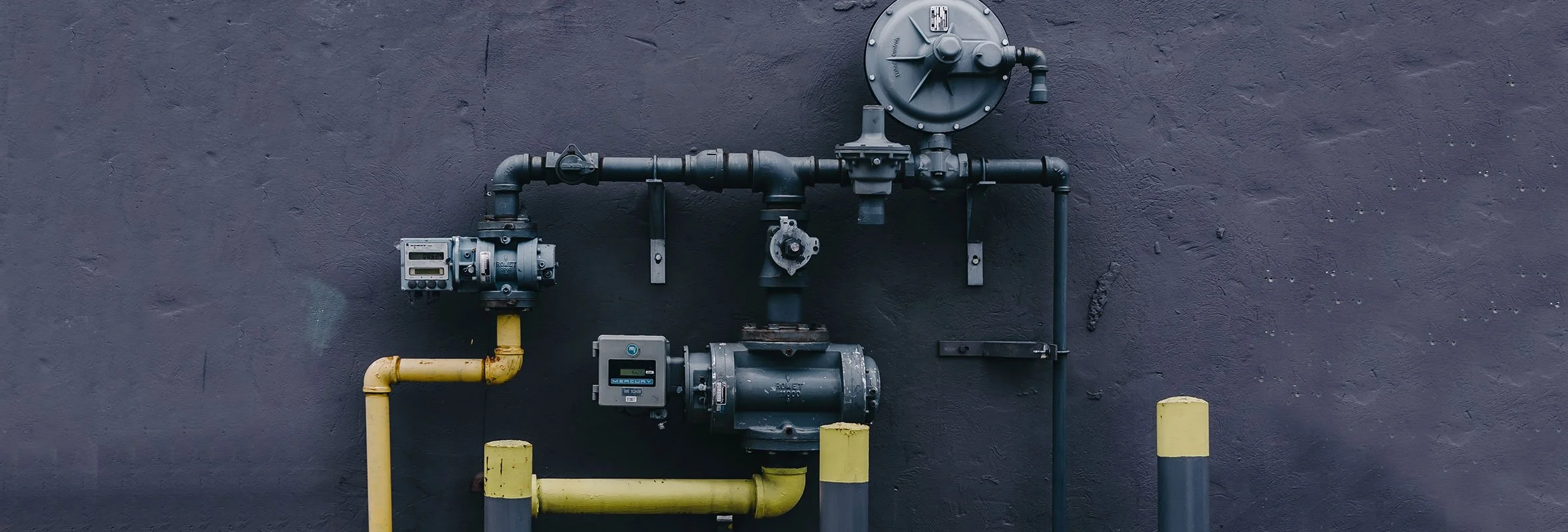 Industrial gas pipes with valves and meters mounted on a wall.