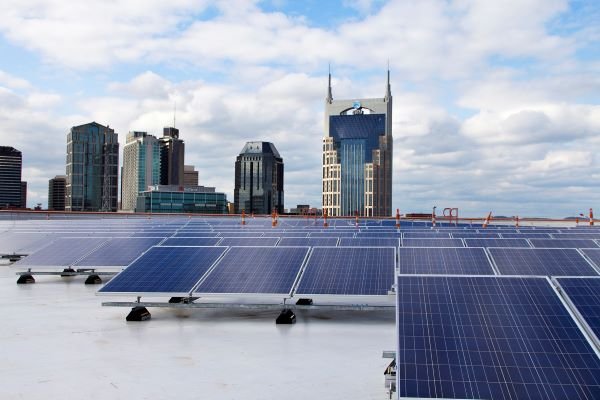 Rooftop solar panels with a city skyline in the background under a cloudy sky.