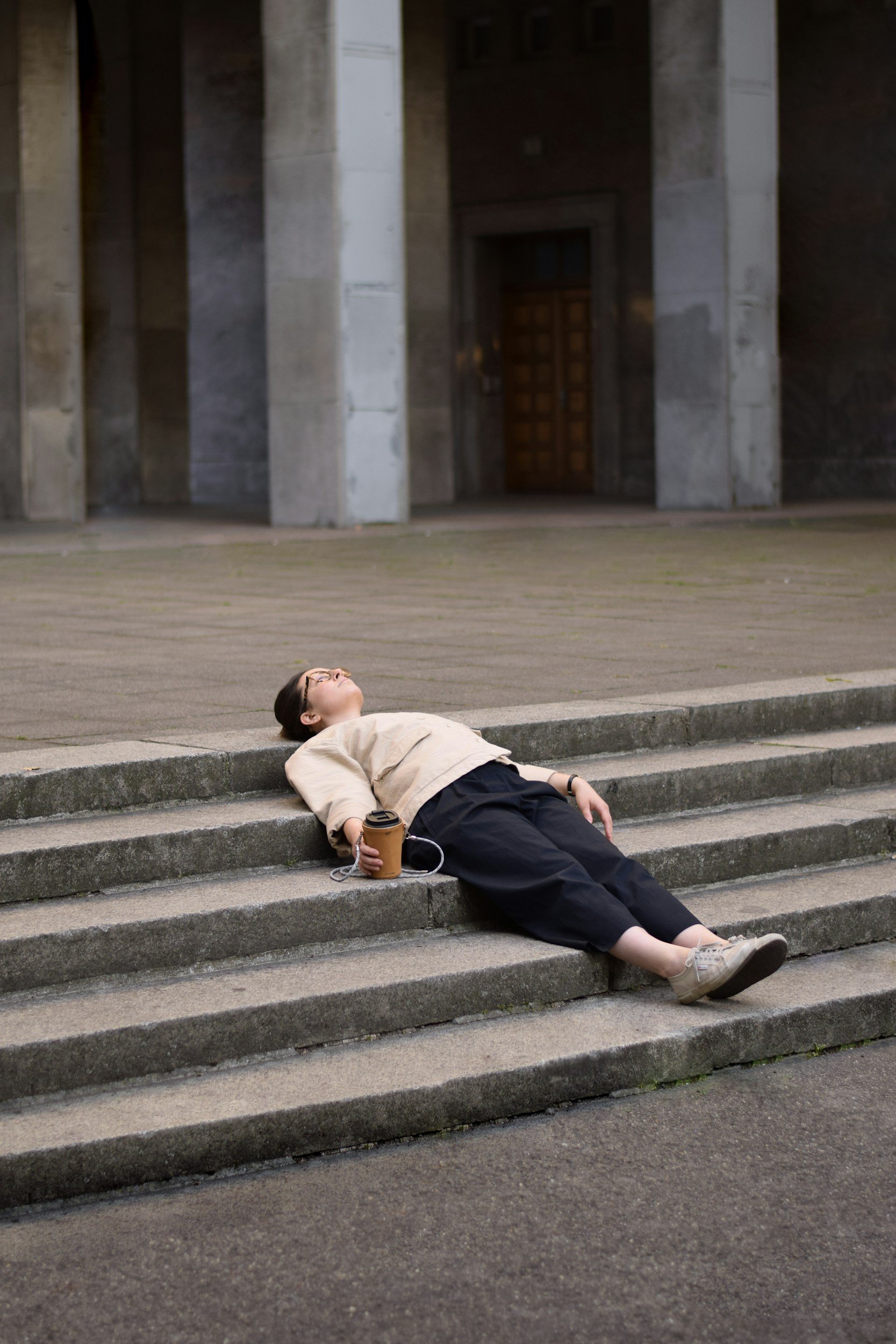 Femme allongée sur des marches d'escalier, une tasse de café à la main.