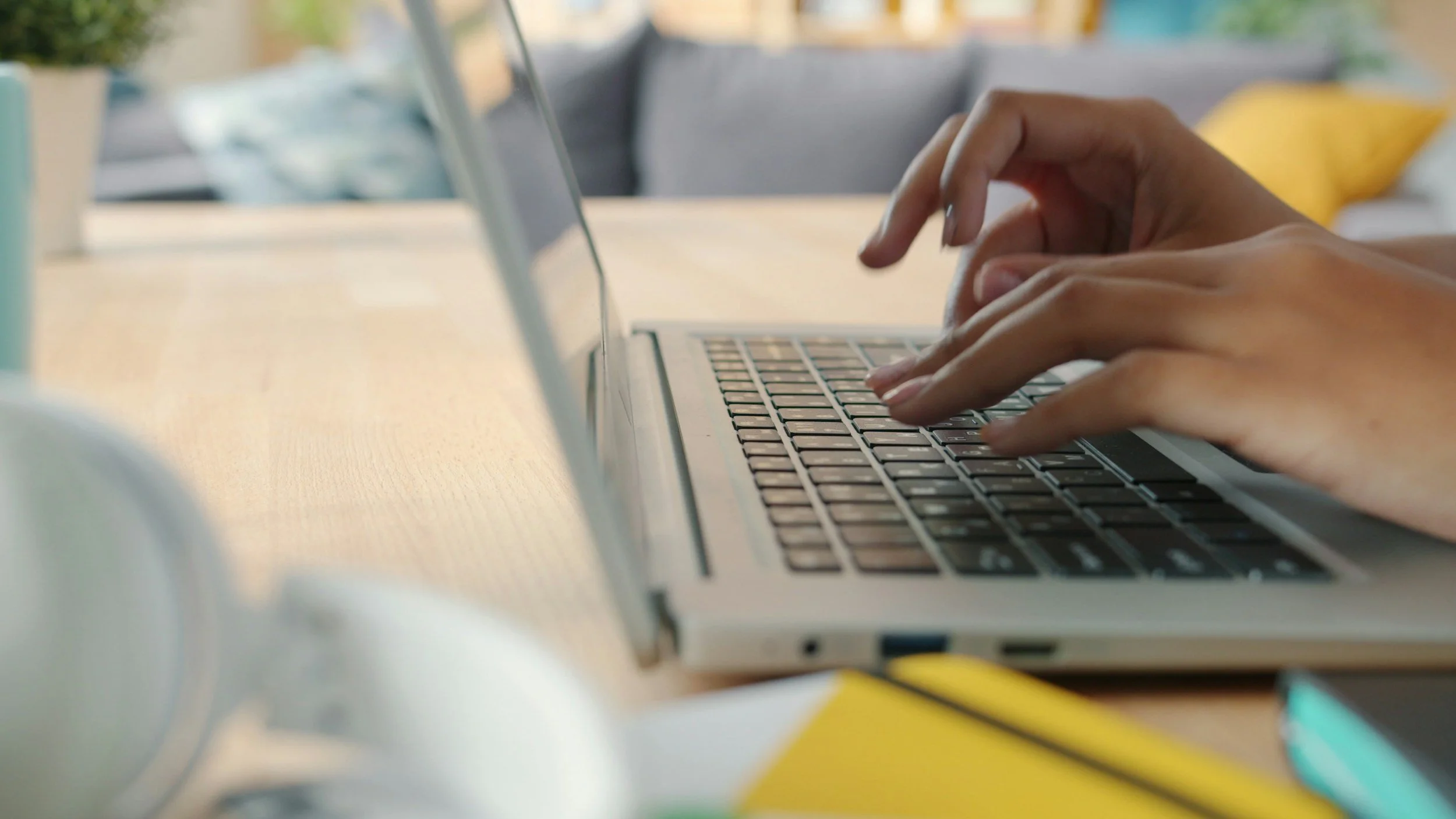 Close-up of hands typing on a laptop keyboard on a wooden desk with blurred background.