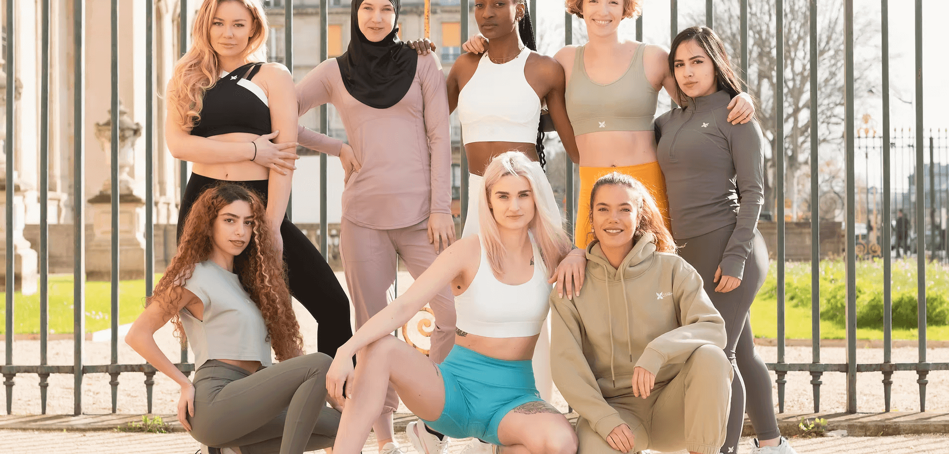 Group of diverse women in activewear posing outdoors near a metal fence