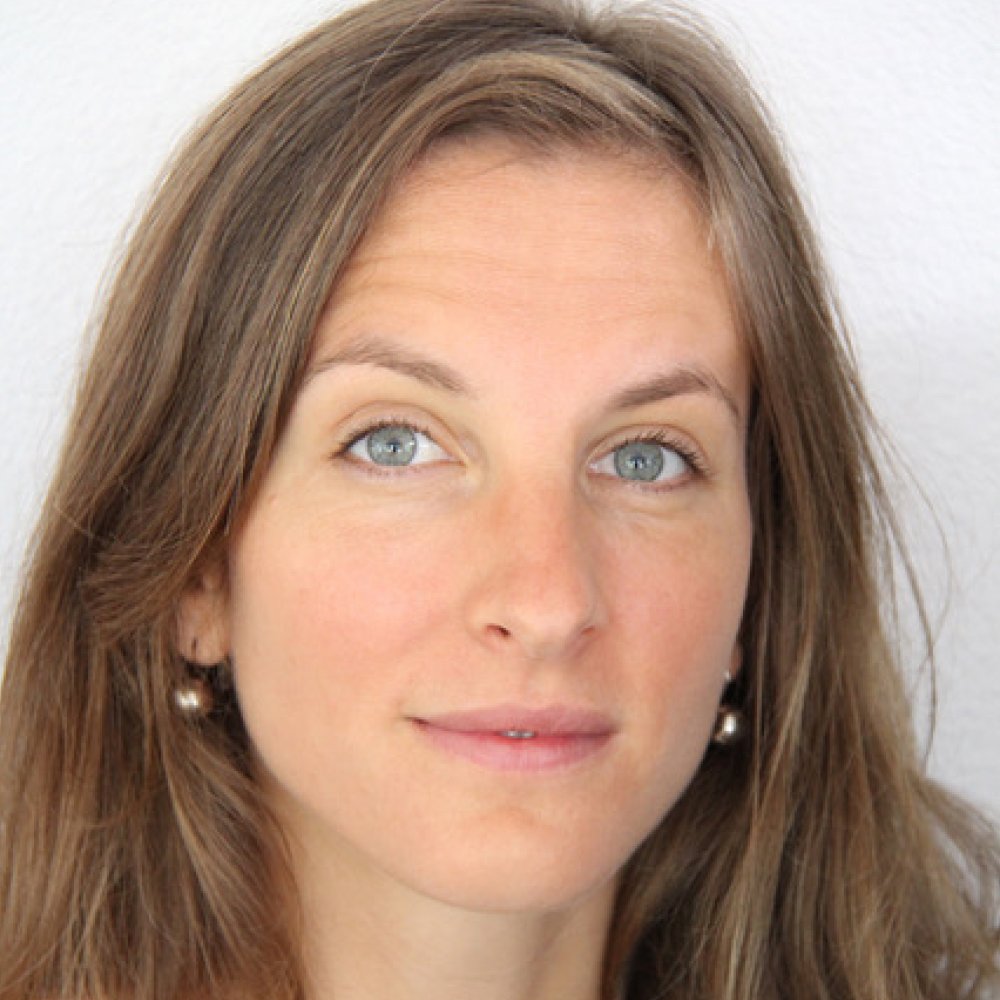 Close-up of a woman with light skin, blue eyes, and light brown hair, wearing pearl earrings, against a white background.