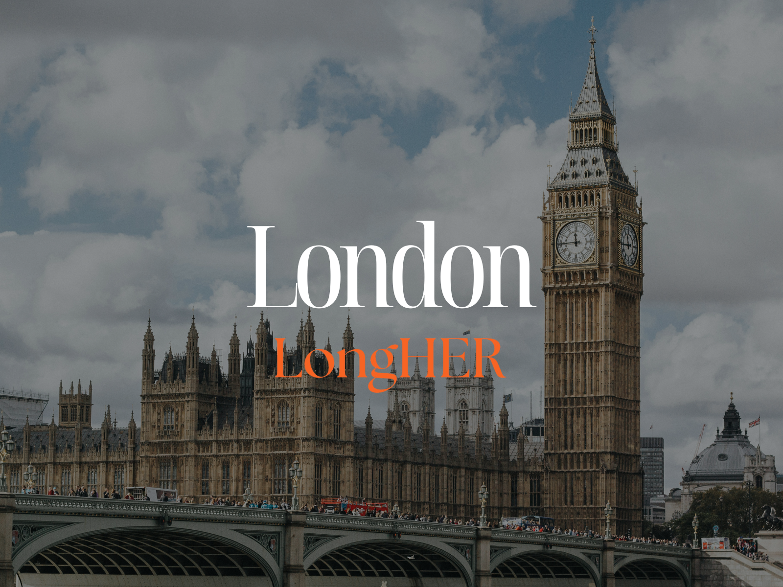 Cityscape with modern building, trees in foreground, snow-capped mountains in background, blue sky with clouds.