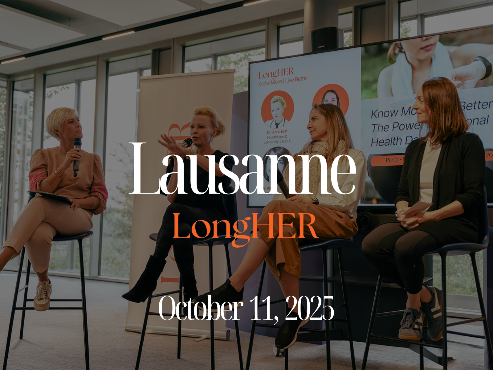 Cityscape with modern building, trees in foreground, snow-capped mountains in background, blue sky with clouds.