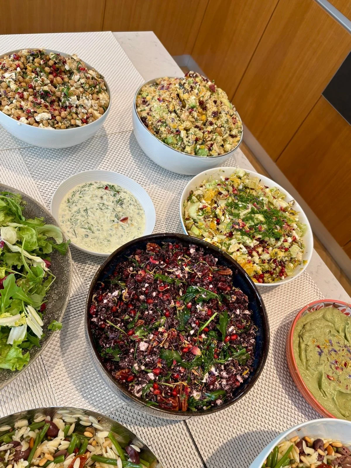 A variety of salads in bowls on a table, including a mixed greens salad, a creamy herb dressing, a beet and berry salad, a chopped vegetable salad, and a guacamole.