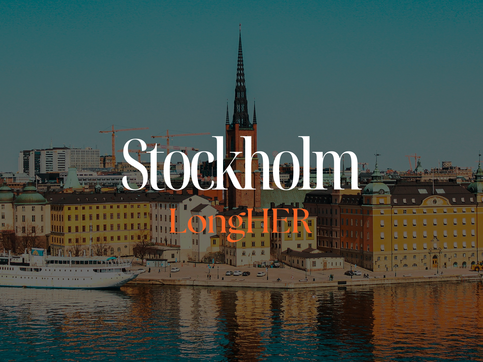 Panoramic view of a city waterfront with colorful historic buildings, a white boat on the water, and a tall church steeple against a blue sky.