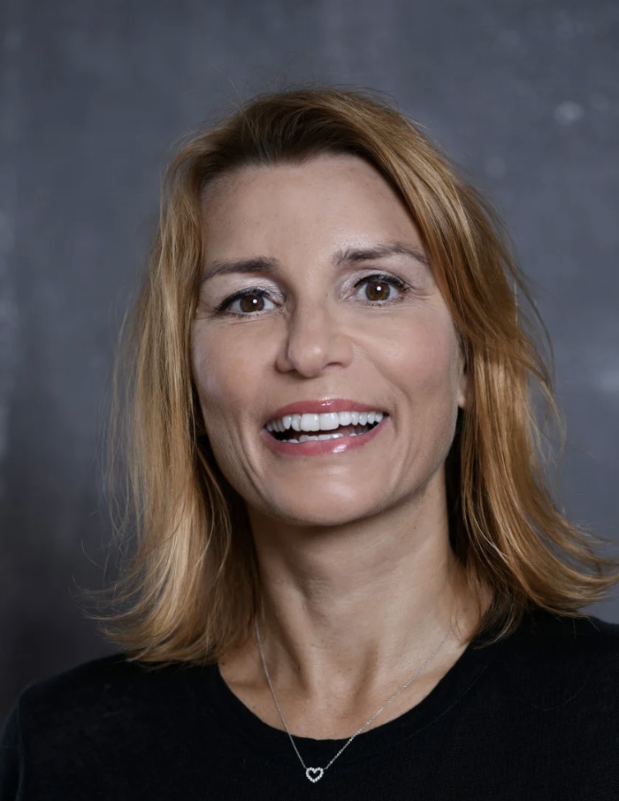 Middle aged woman with blonde hair and smiling against grey background
