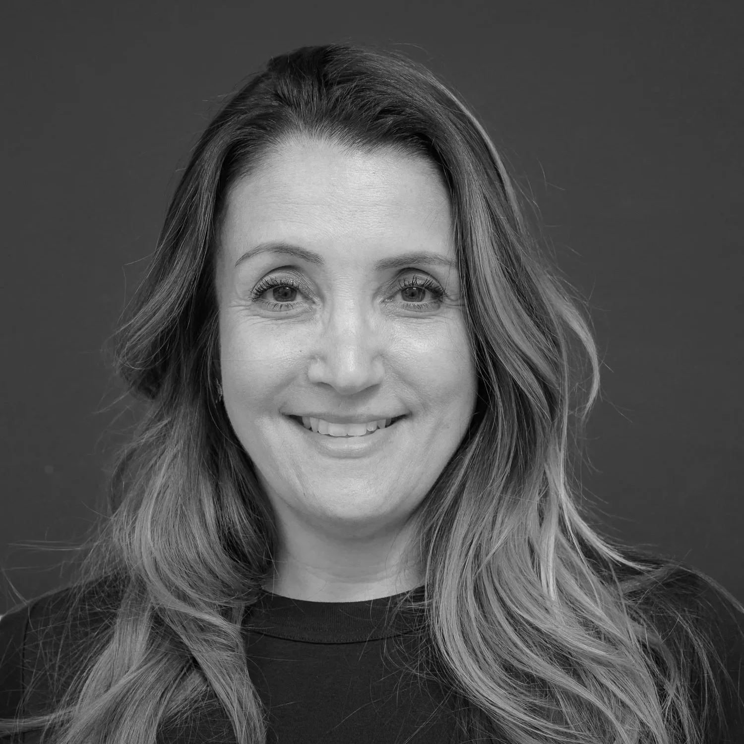 Black and white portrait of a woman with long wavy hair, smiling, facing forward.